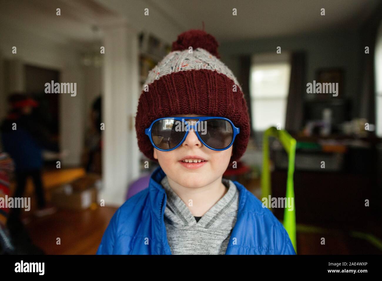 Mid shot of boy wearing blue sunglasses and winter hat indoors at home Stock Photo