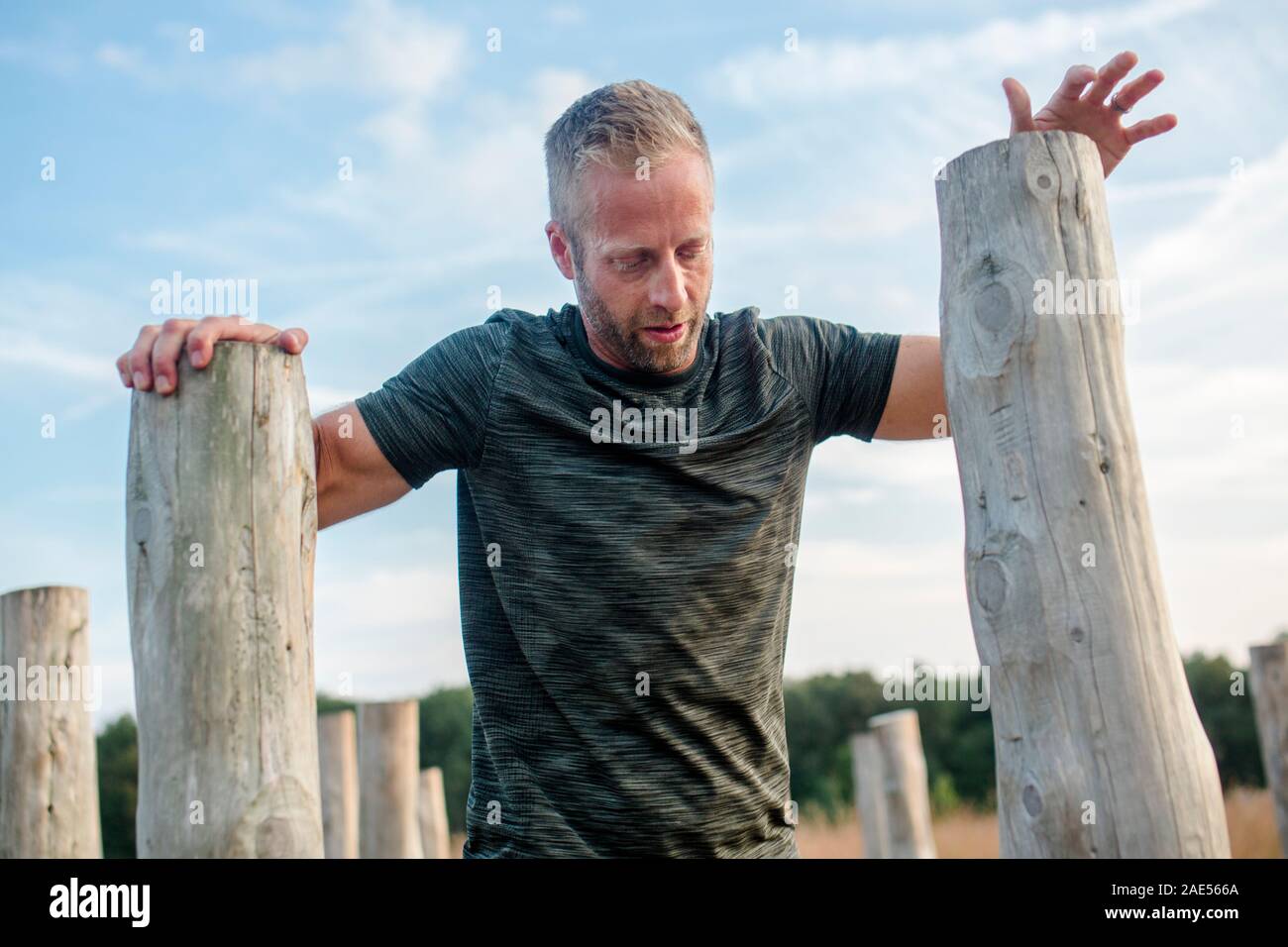 Top-half of man leaning on wood poles on obstacle course Stock Photo