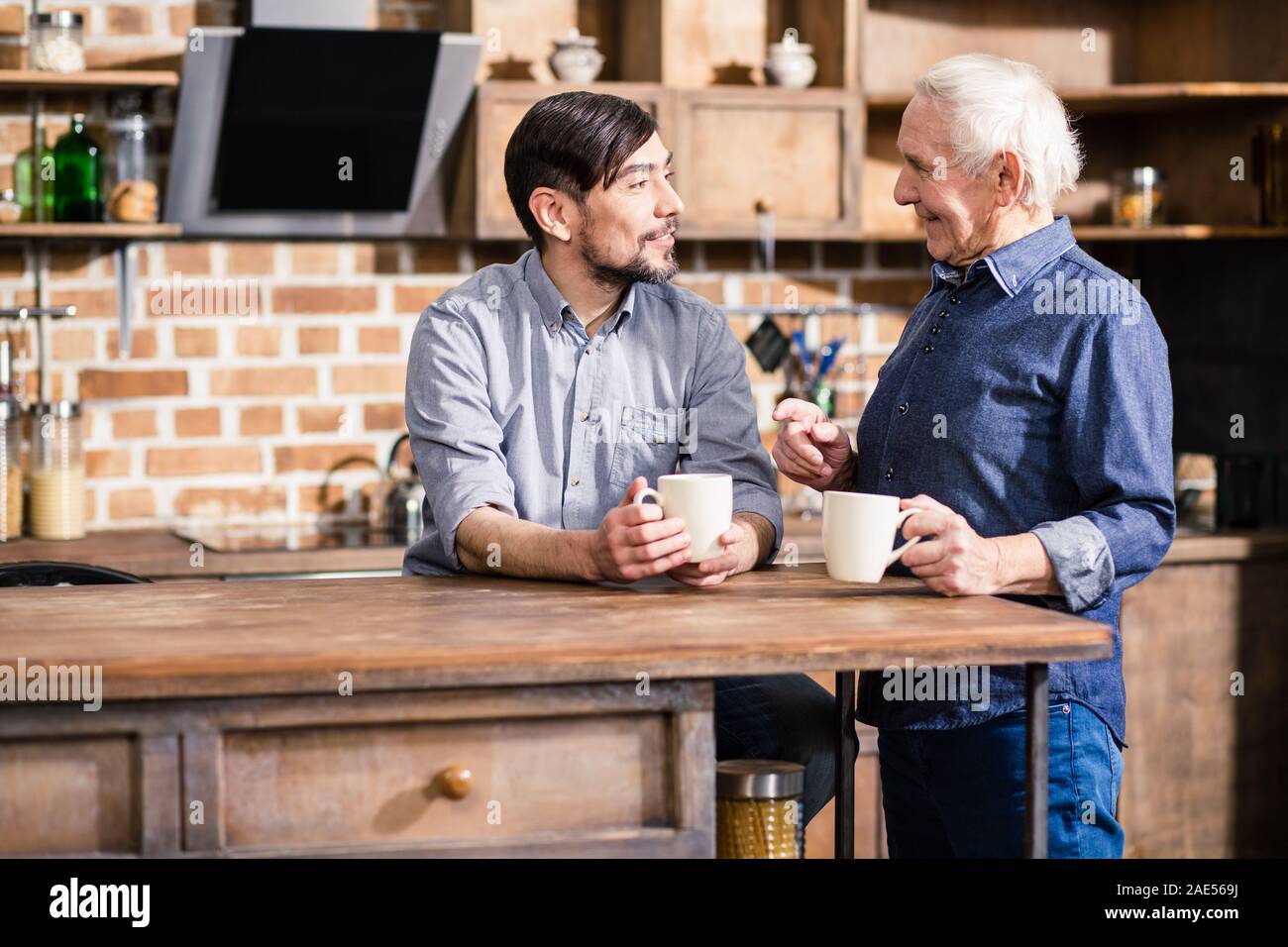 Positive man drinking coffee with his elderly father Stock Photo