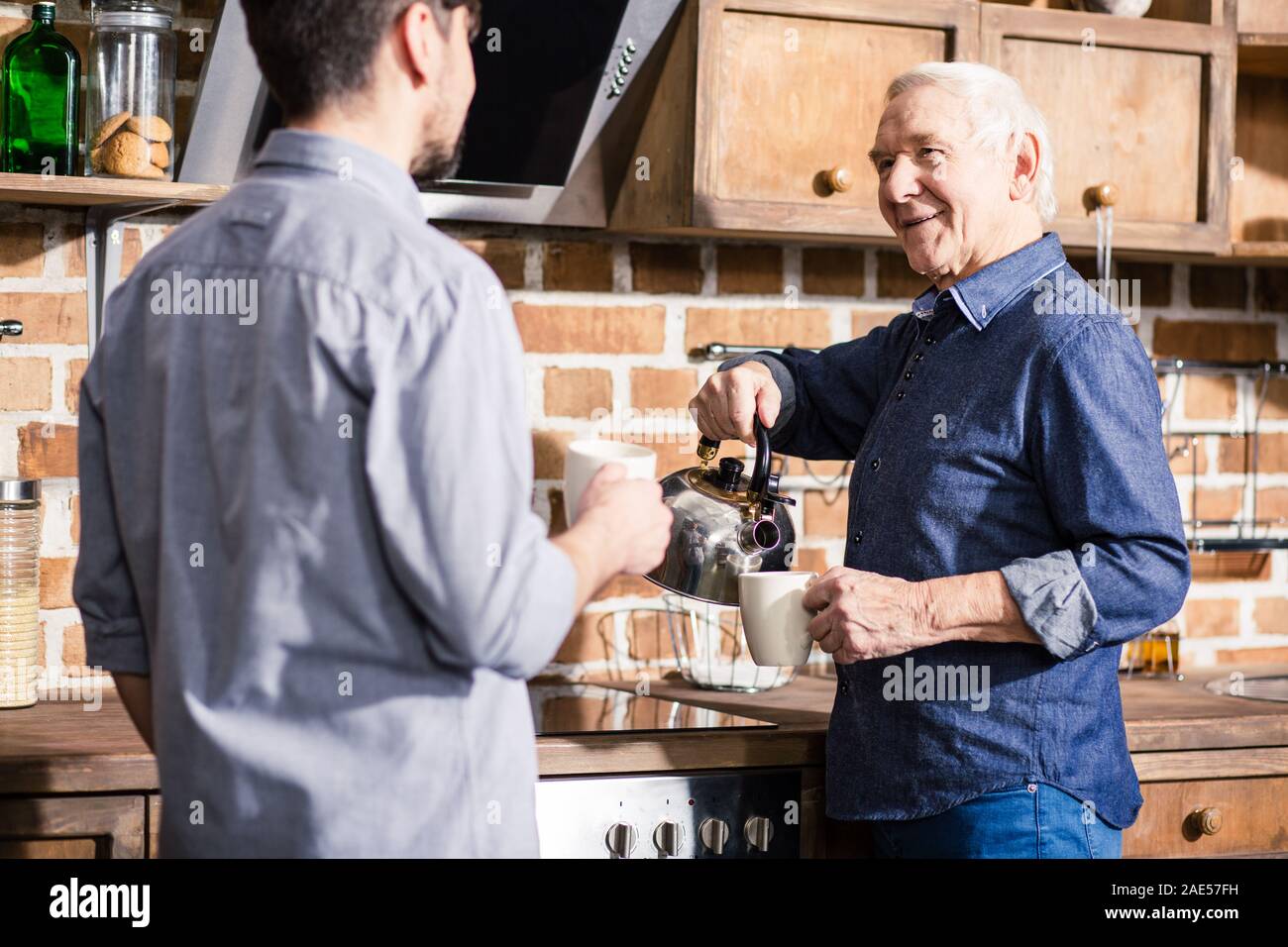 Positive elderly man drinking tea with his son Stock Photo