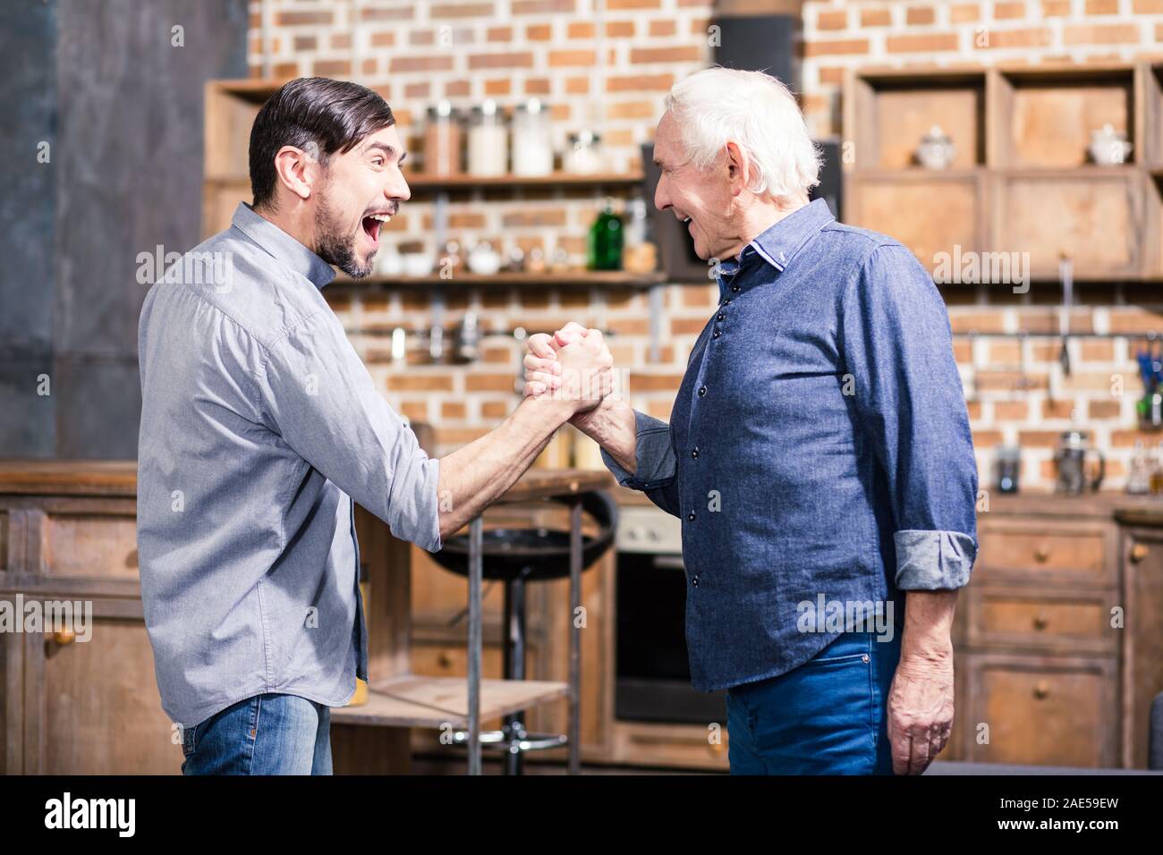 Positive aged man and his son practicing arm wrestling Stock Photo