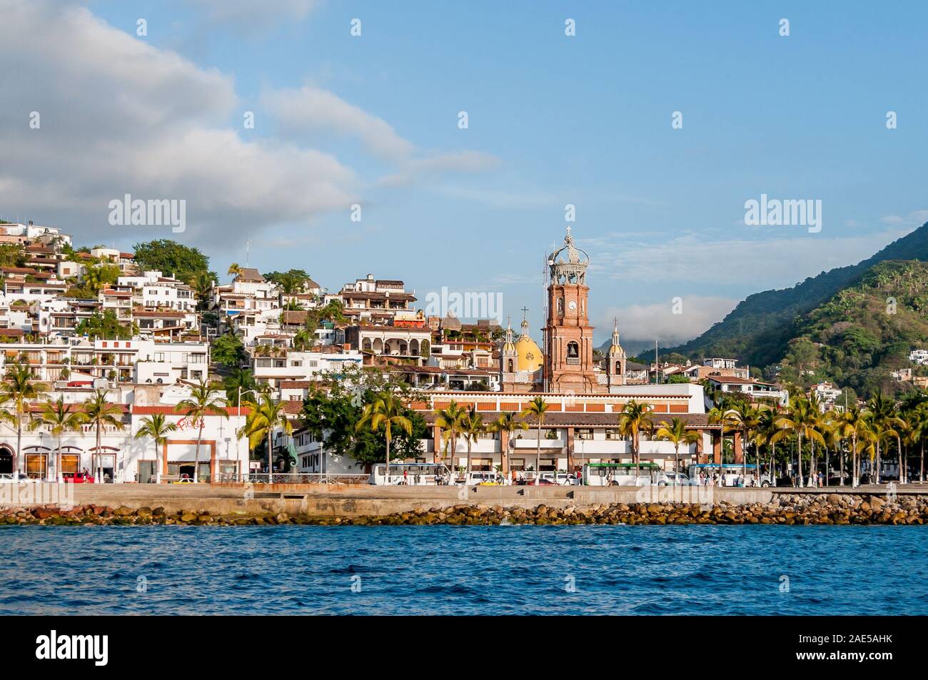 View of downtown Puerto Vallarta as seen from water, Our Lady of Guadalupe church bell towers and gold dome, pedestrians on the malecon waterfront. Stock Photo