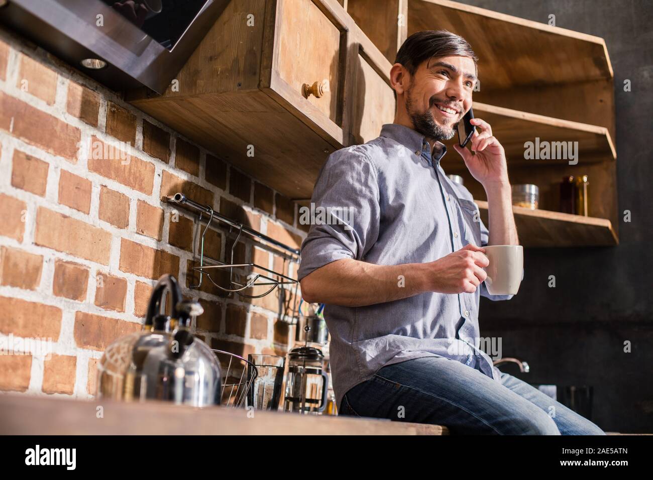 Positive man talking on phone in the kitchen Stock Photo