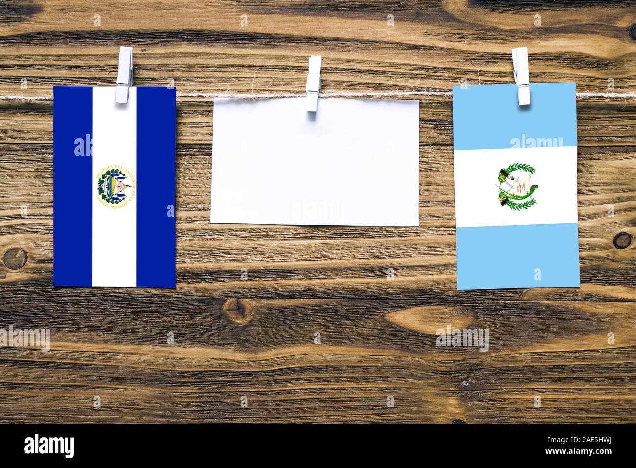 Hanging flags of El Salvador and Guatemala attached to rope with clothes pins with copy space on white note paper on wooden background.Diplomatic rela Stock Photo