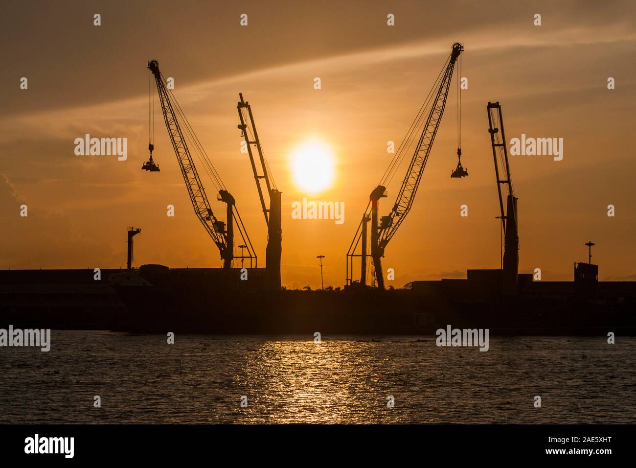 Industrial cranes silhouetted against the sunset in Barranquilla, Colombia. Stock Photo