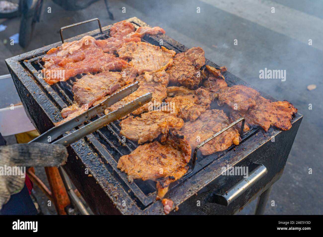 Human hand using tongs while grilling pork chop on coal Stock Photo Alamy