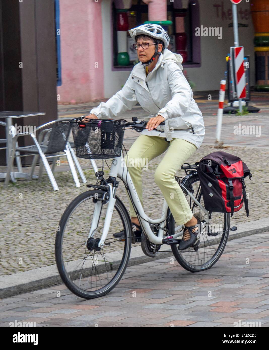 Caucasian woman riding bicycle with pannier and handlebar basket commuting in Magdeburg Saxony-Anhalt Germany. Stock Photo