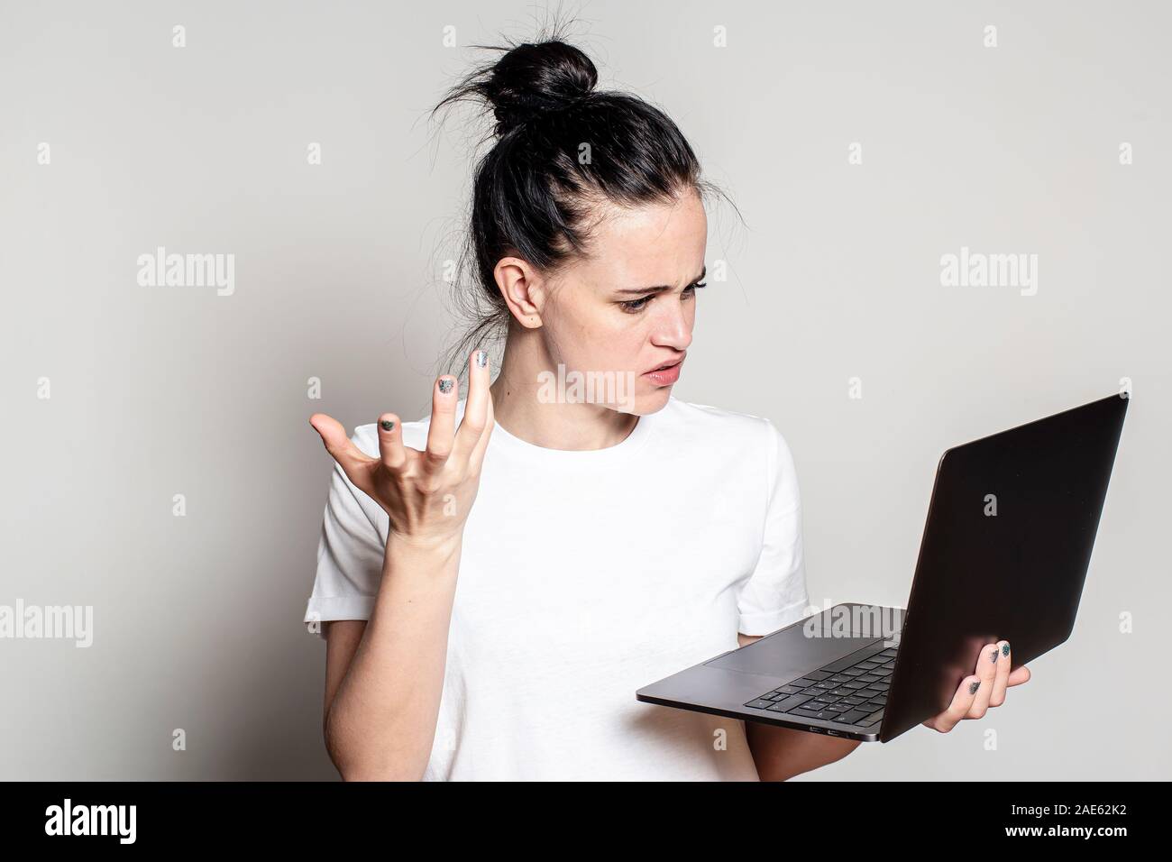 Student upset, bewildered looks at his laptop, frowns and makes a gesture with hand. Stock Photo