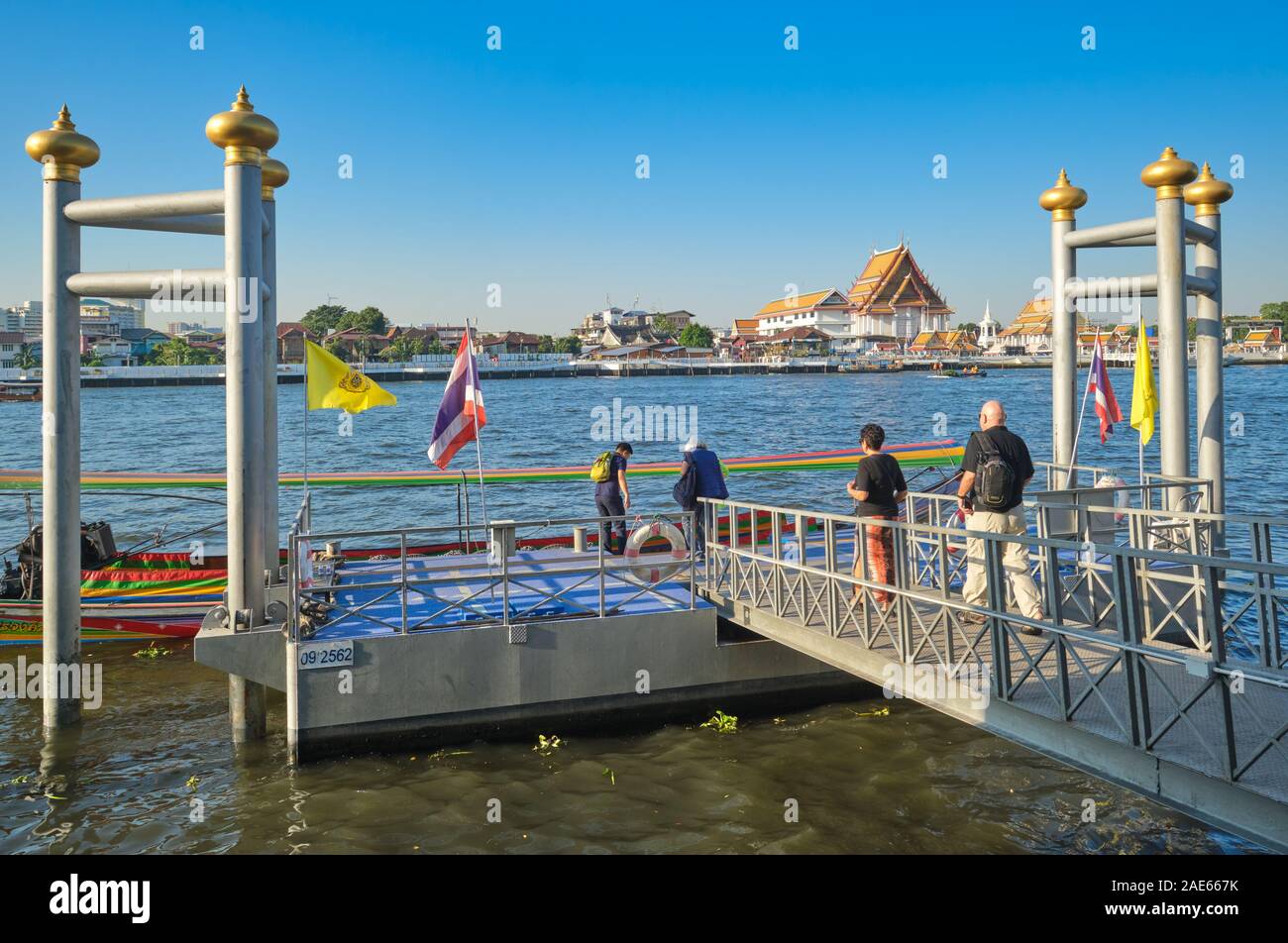 A group of Western tourists boarding a longtail boat at Atsadang / Yodpiman Pier by the Chao Phraya River in Bangkok, Thailand; b/g: Wat Kalayanamit Stock Photo