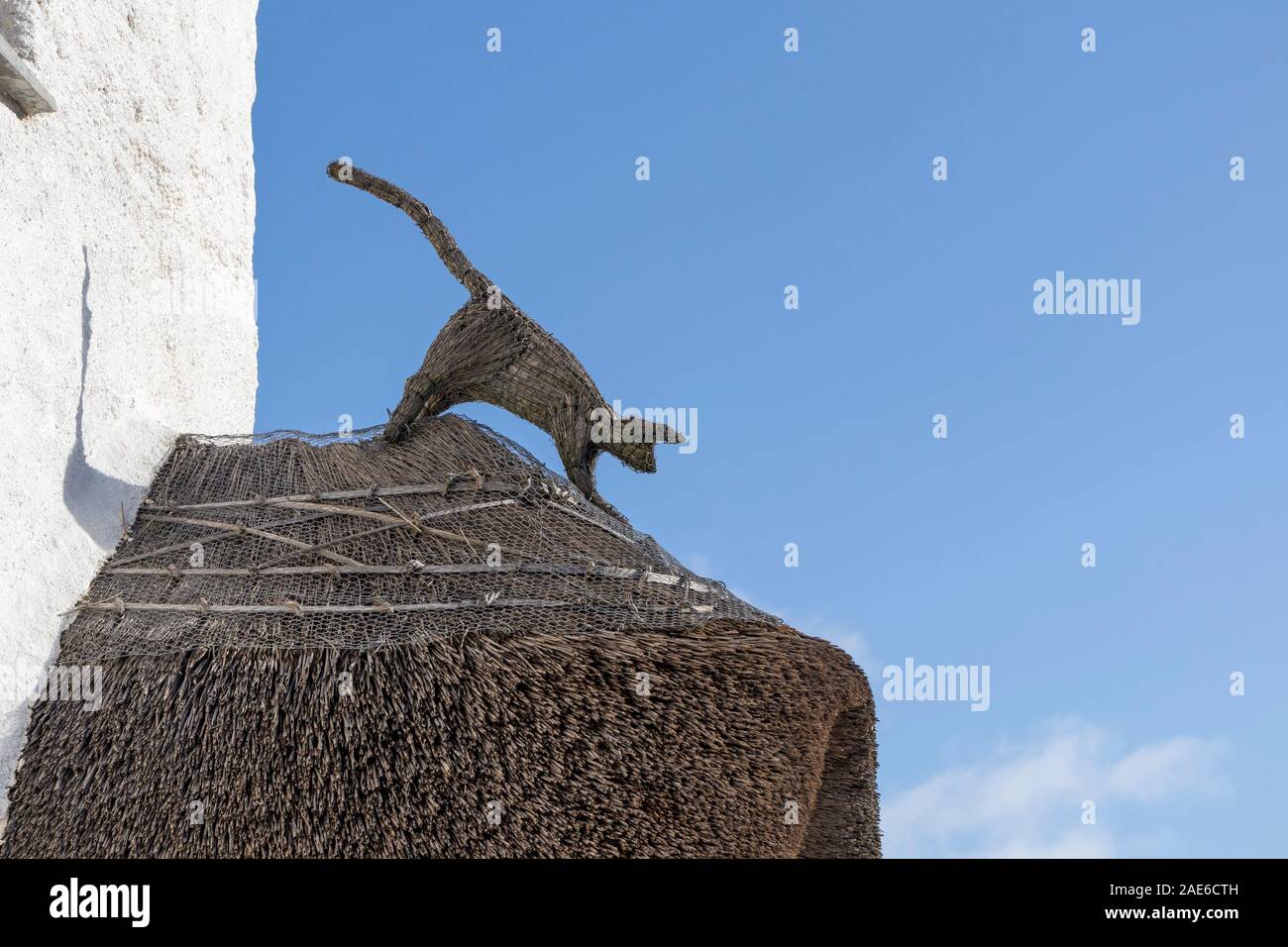 Decorative Thatched Cat Finial on the Thatched Roof of the Mariners Cottages in Church Cove with the View out to Sea, Lizard, Cornwall, UK Stock Photo
