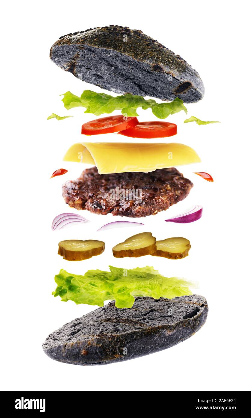 Delicious hamburger with bread of black color isolated on a white background. Freshly baked burger with flying ingredients Stock Photo