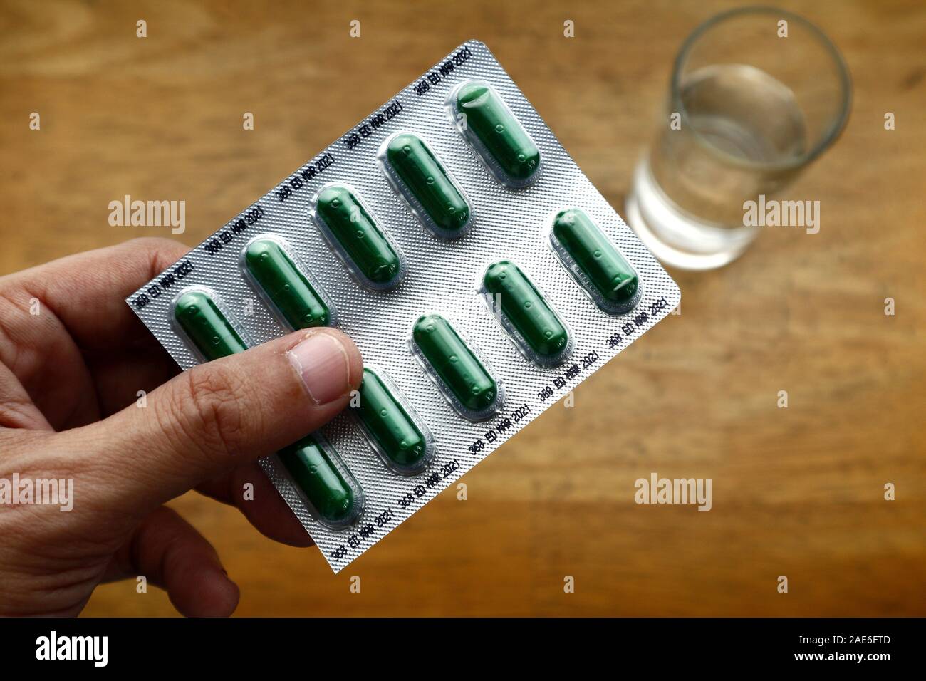 Photo of hand holding a foil pack filled with herbal cough medicine and glass water on a wooden table Stock Photo