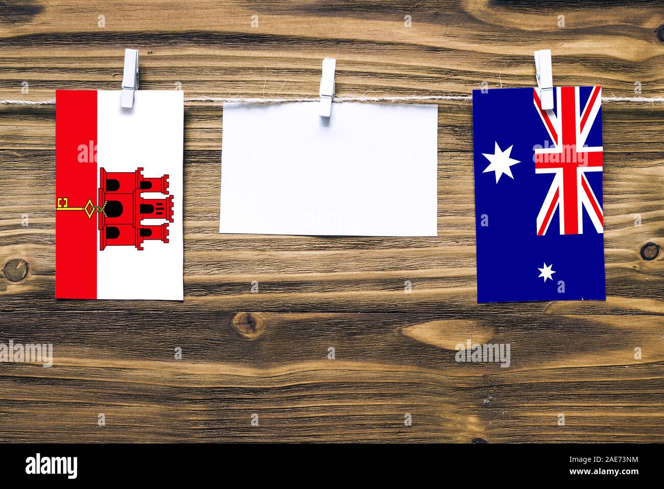 Hanging flags of Gibraltar and Heard and Mcdonald Islands attached to rope with clothes pins with copy space on white note paper on wooden background. Stock Photo