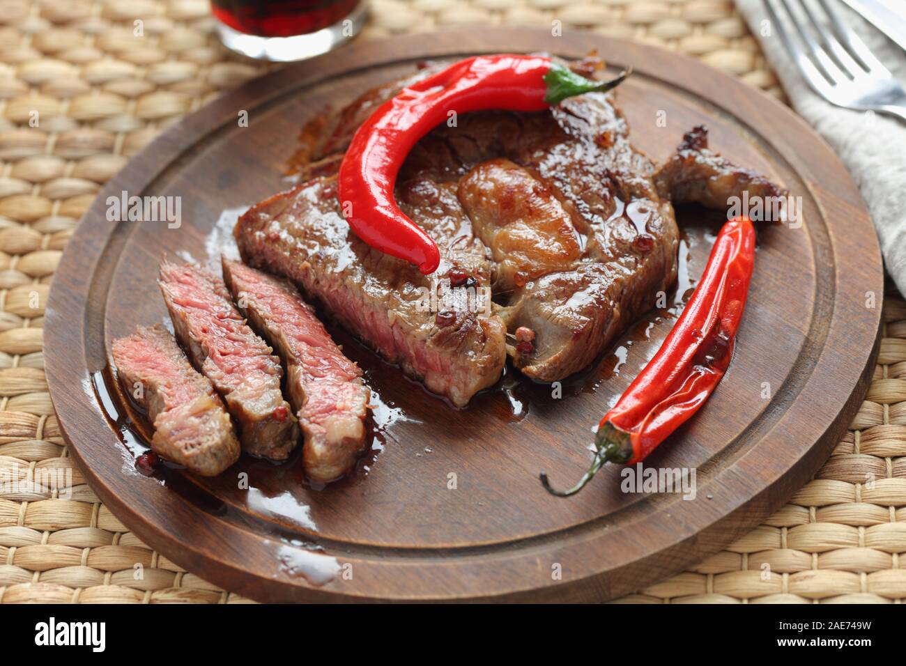 Sliced medium rare beef steak topped with roasted chili pepper on a wooden cutting board Stock Photo