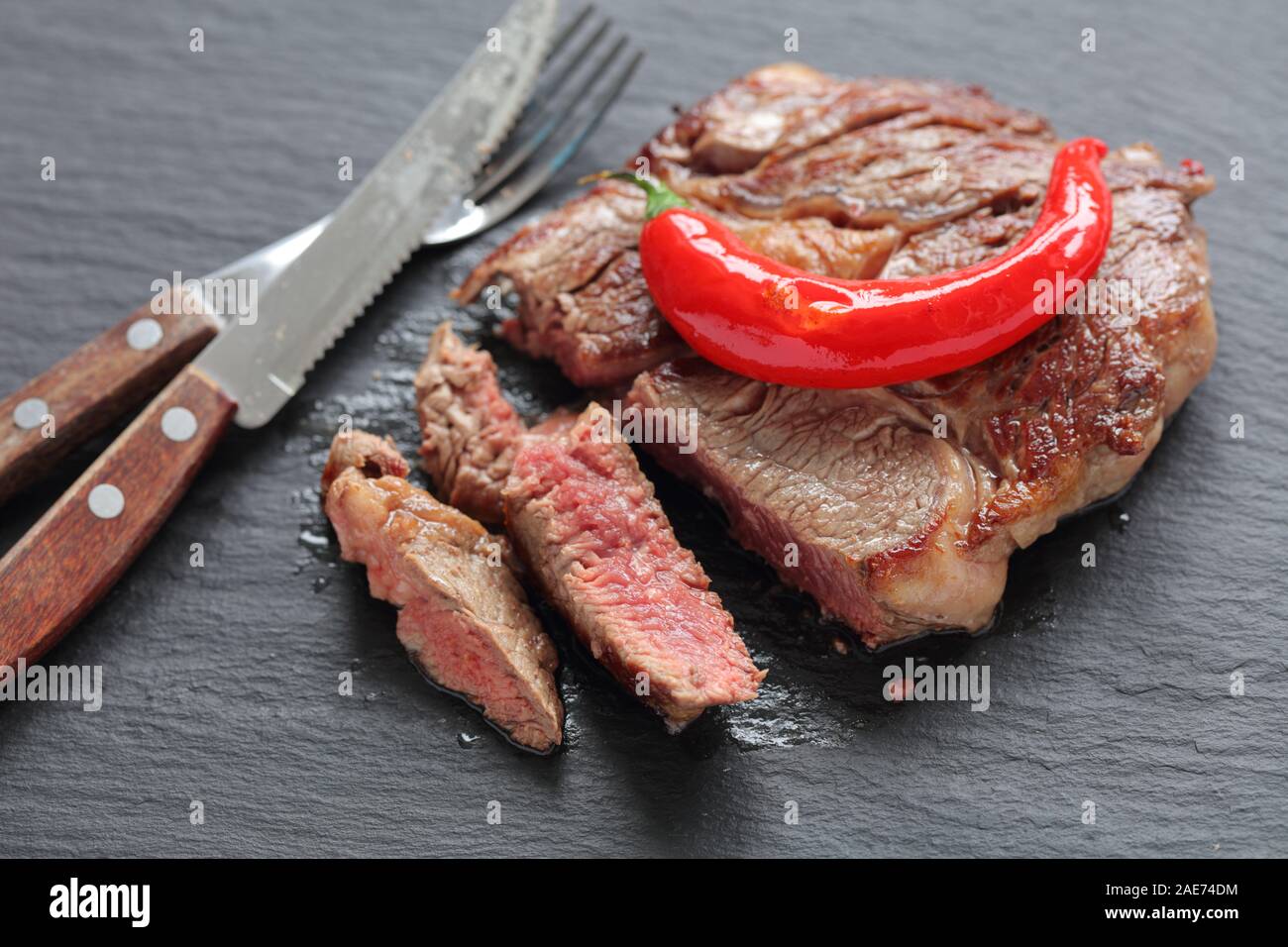 Sliced medium rare beef steak topped with roasted chili pepper on a slate tray closeup Stock Photo