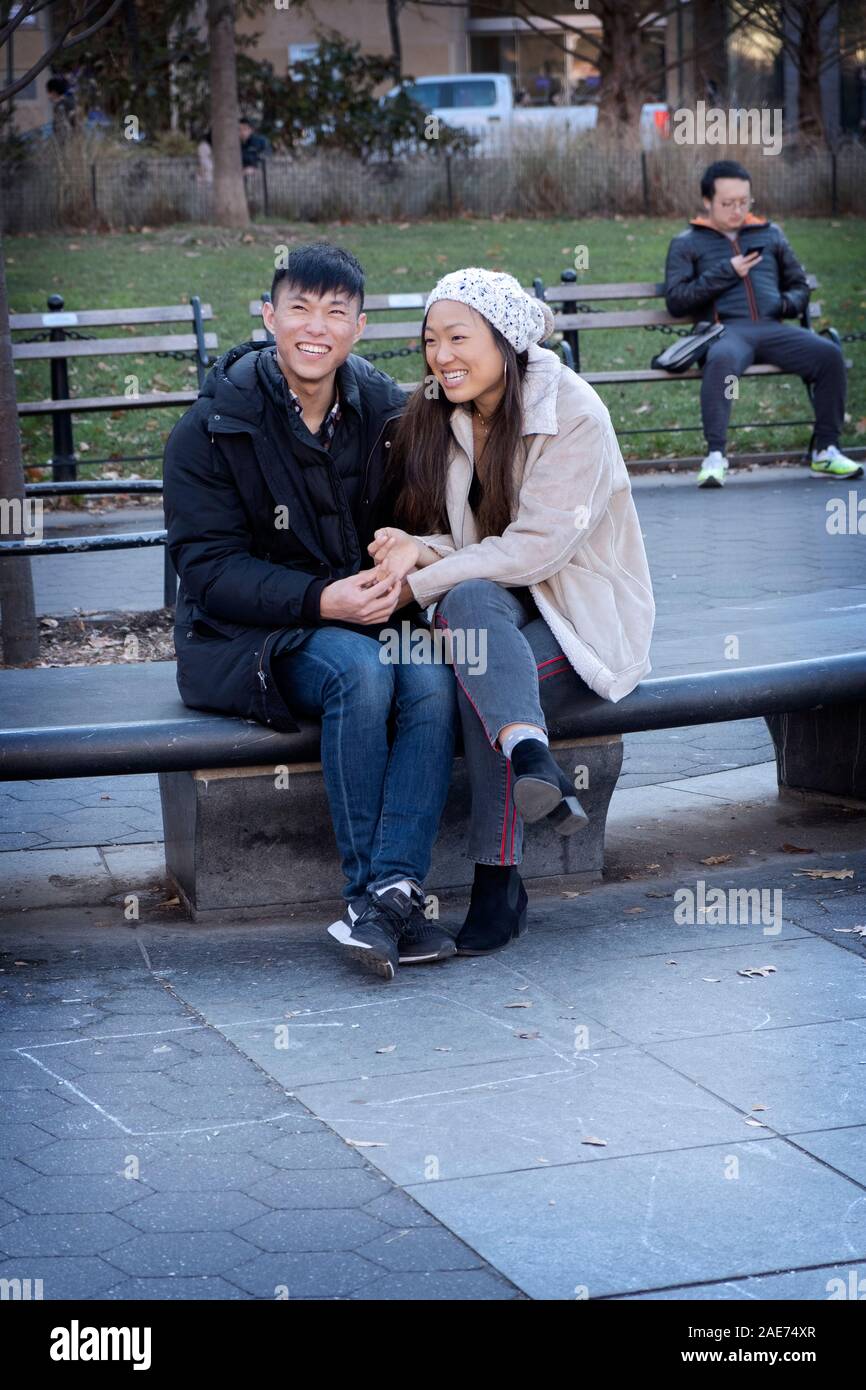 A affectionate Asian couple share a laugh while sitting on a bench in Washington Square Park in Manhattan, New York City. Stock Photo