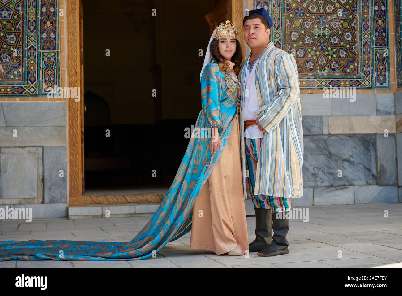 bridal couple in traditional clothes posing in front of famous Registan Square, Samarkand, Uzbekistan, Central Asia Stock Photo