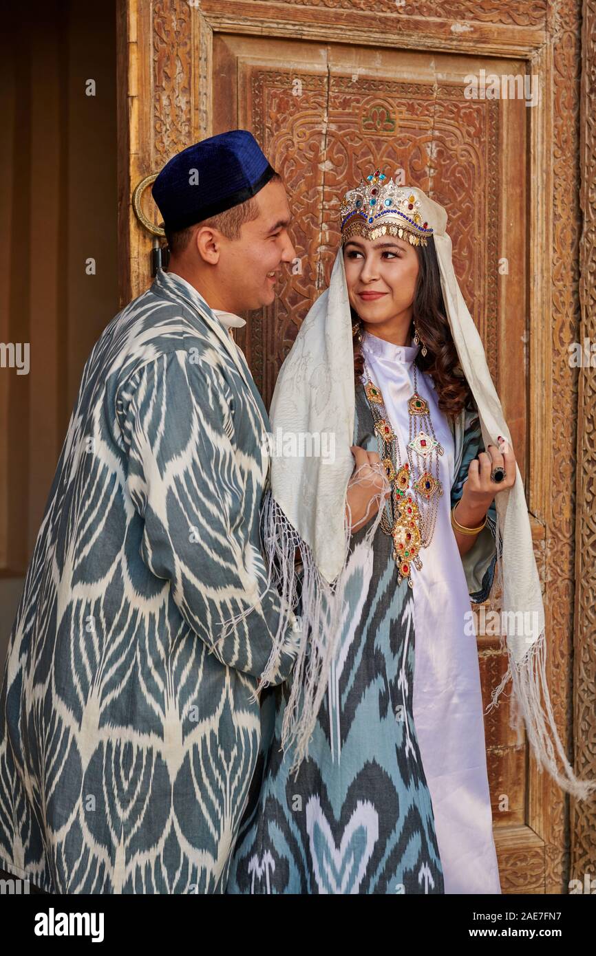 bridal couple in traditional clothes posing in front of famous Registan Square, Samarkand, Uzbekistan, Central Asia Stock Photo
