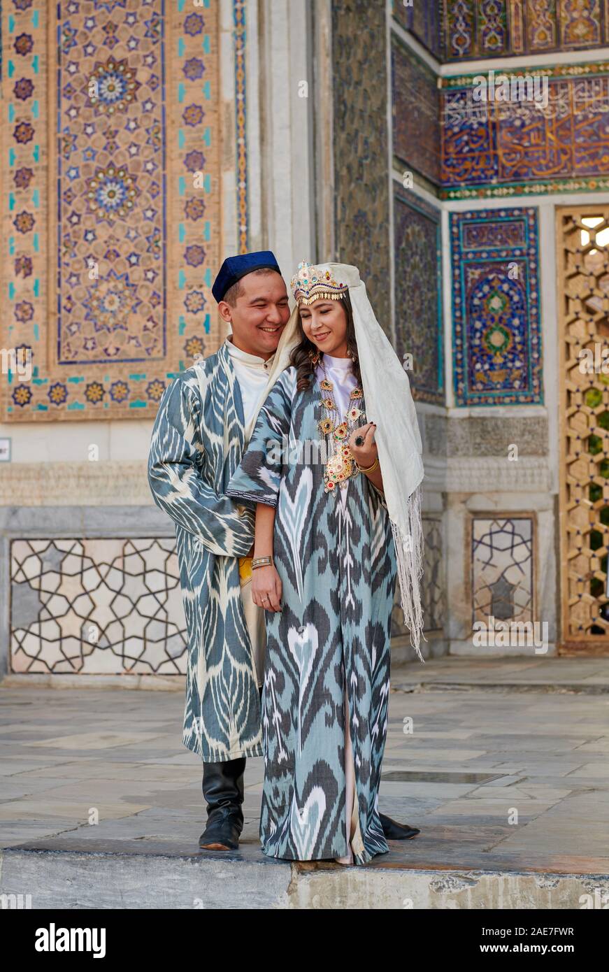 bridal couple in traditional clothes posing in front of famous Registan Square, Samarkand, Uzbekistan, Central Asia Stock Photo