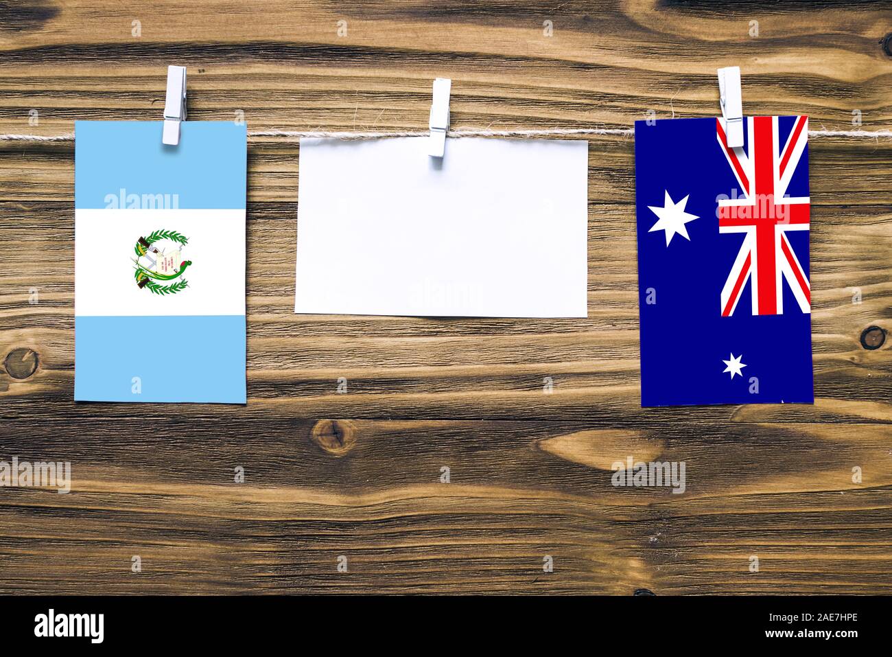 Hanging flags of Guatemala and Heard and Mcdonald Islands attached to rope with clothes pins with copy space on white note paper on wooden background. Stock Photo