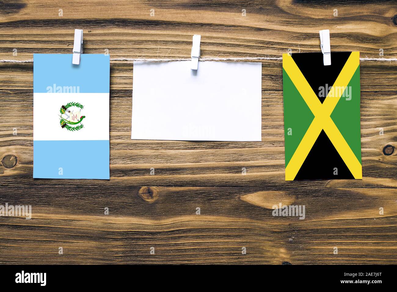 Hanging flags of Guatemala and Jamaica attached to rope with clothes pins with copy space on white note paper on wooden background.Diplomatic relation Stock Photo