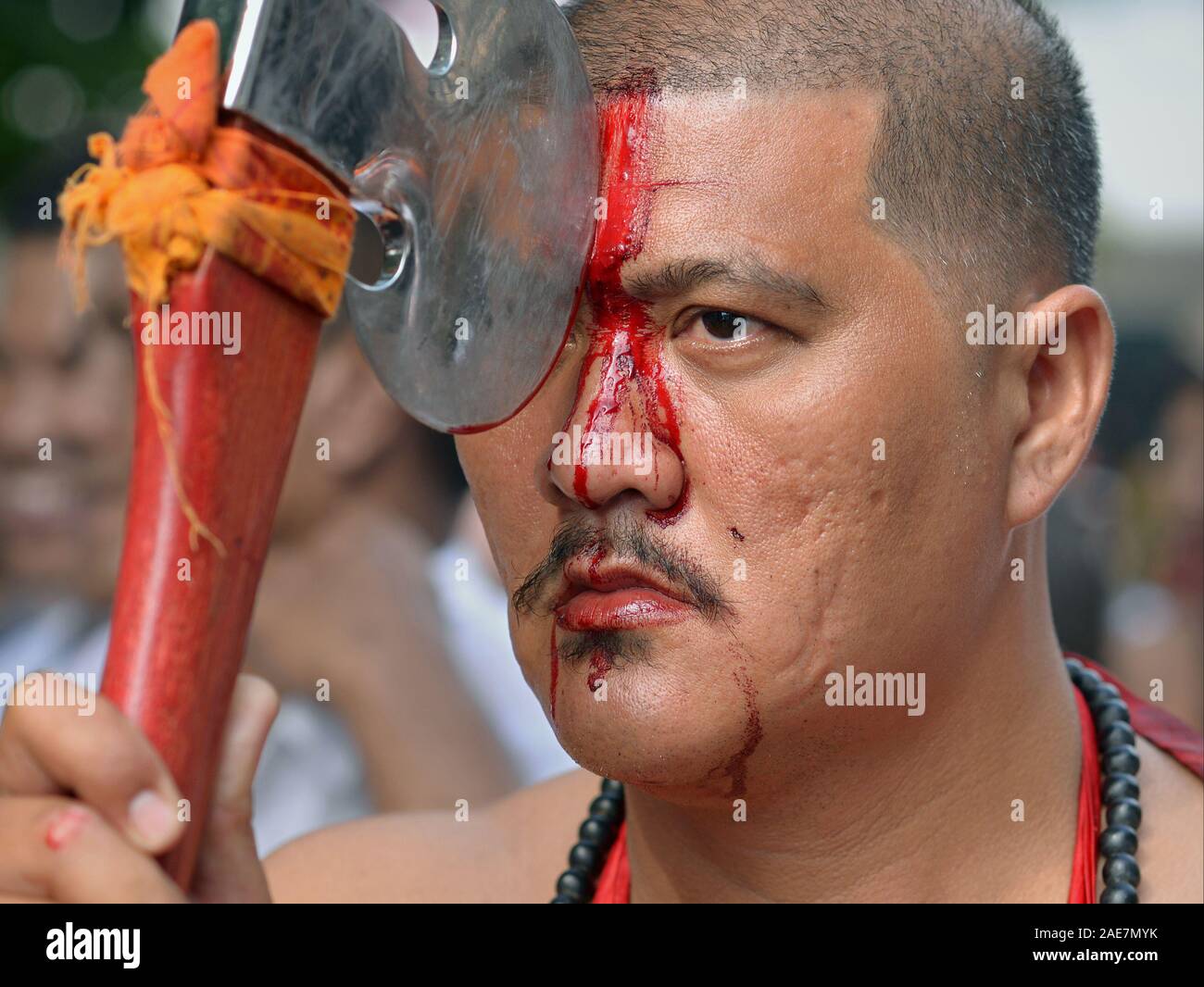 Thai Chinese Taoist devotee cuts his forehead with a sharp axe during the Phuket Vegetarian Festival (Nine Emperor Gods Festival). Stock Photo