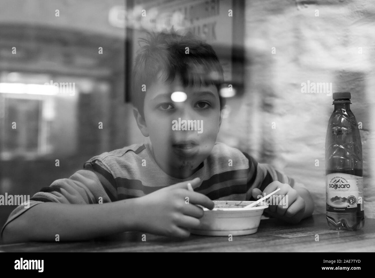 A boy eating pasta from outside a restaurant window, shadows and light