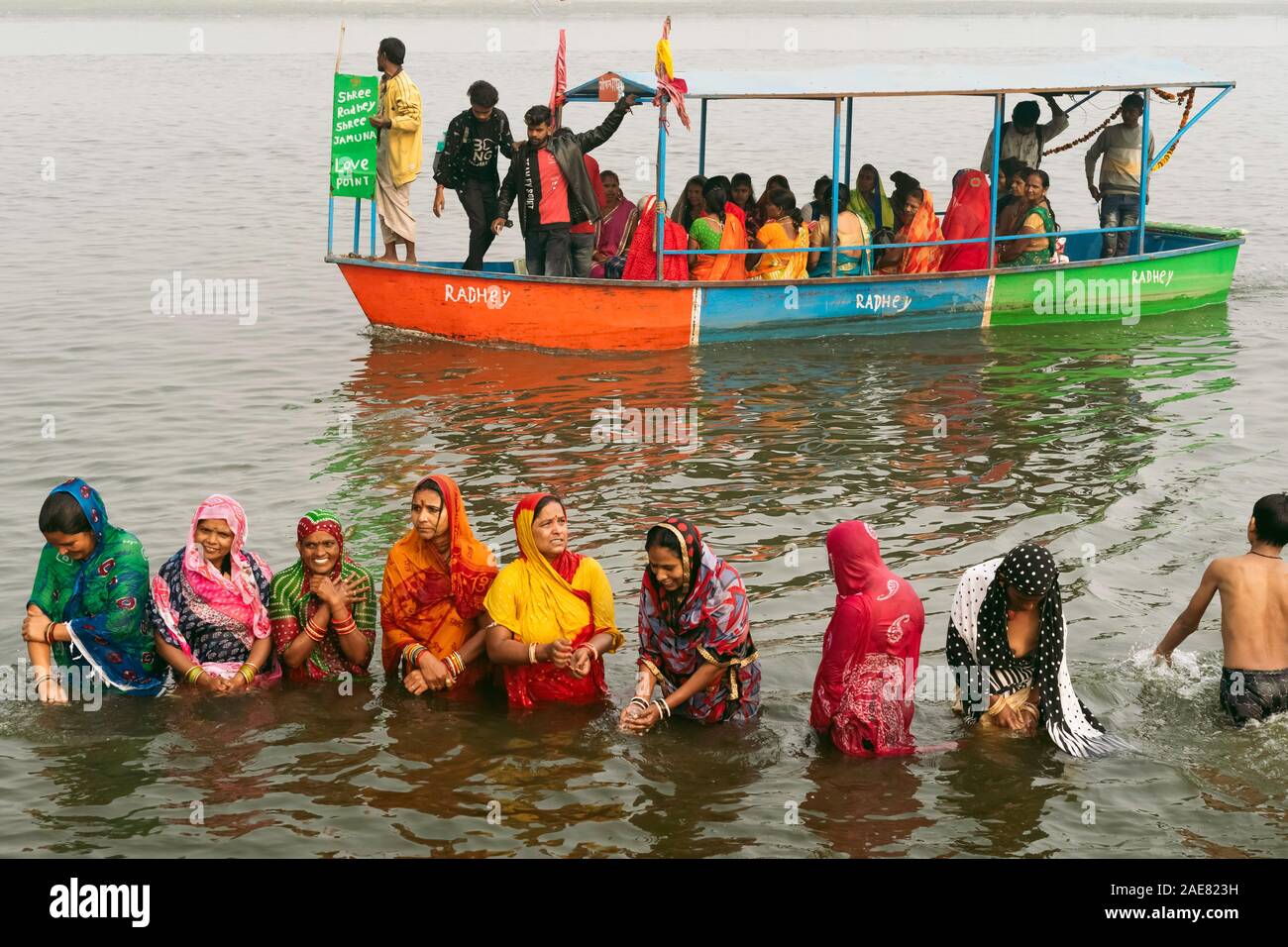 Pilgrims, mainly women, dressed in colorful Indian clothes having a ritual bath in the holy Yamuna river at dawn in Vrindavan, Uttar Pradesh, Stock Photo