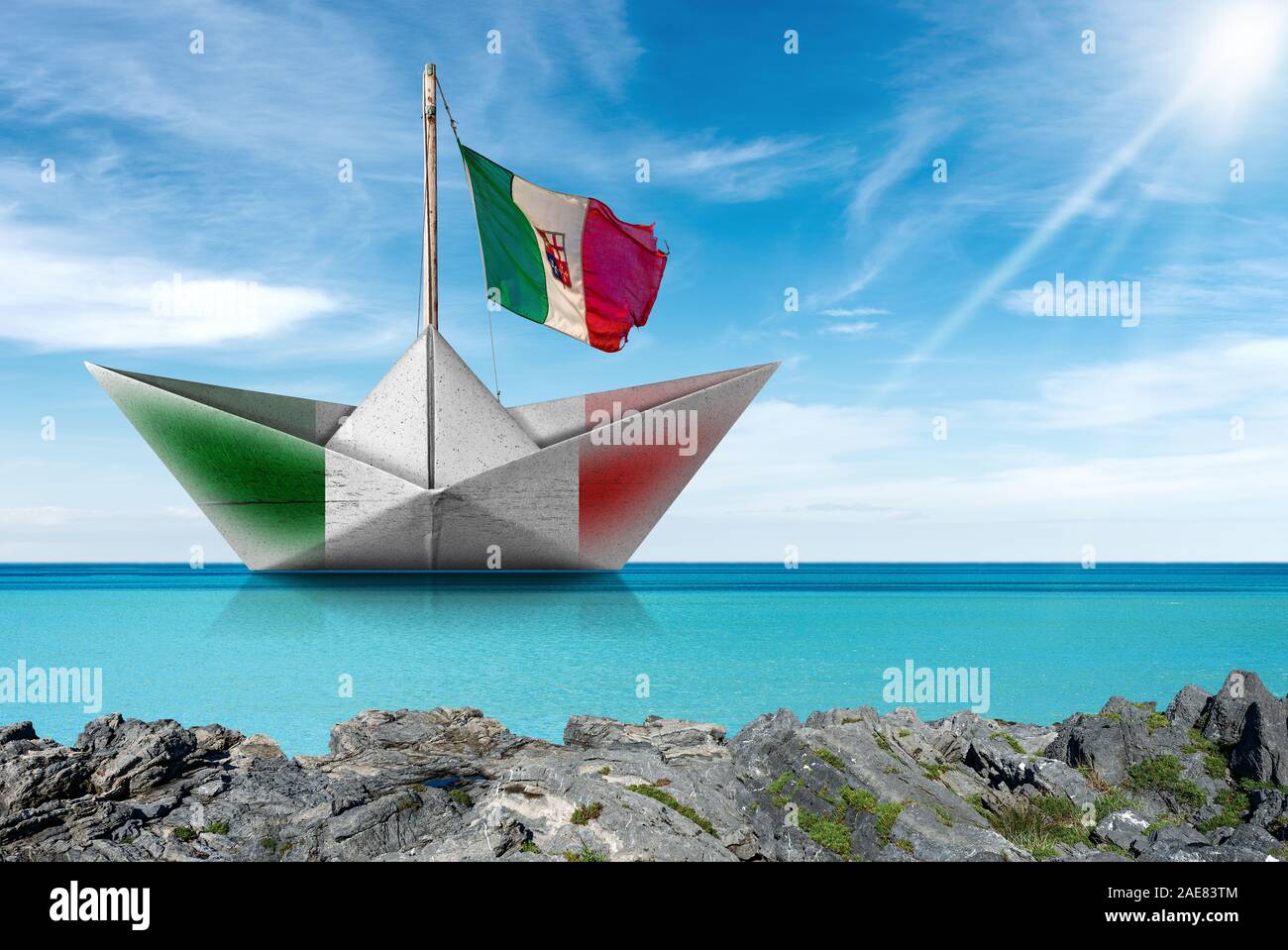 White paper boat with the Italian flag, in a turquoise sea with blue sky, clouds and sun rays, photography Stock Photo