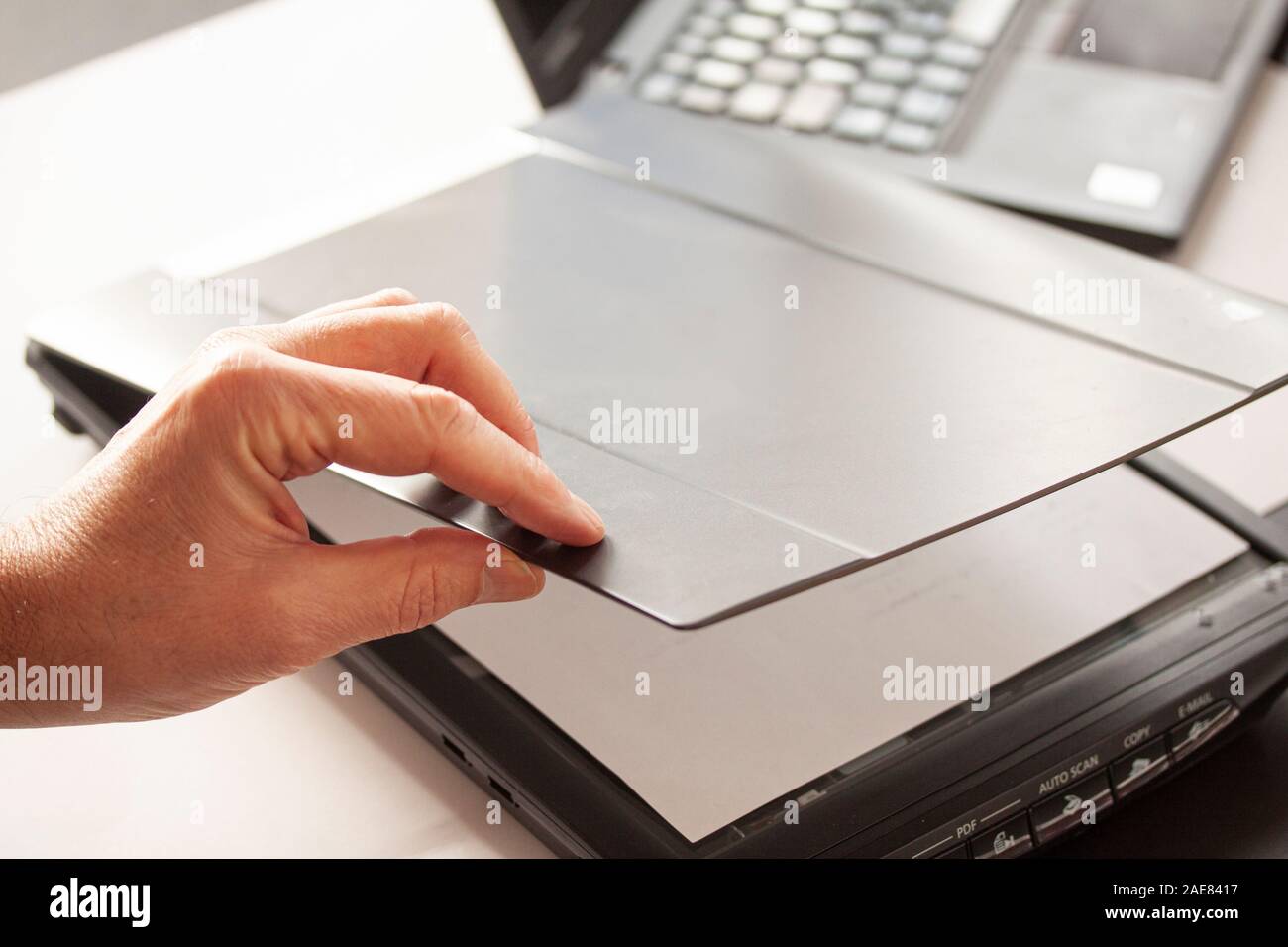 A hand closing a flatbed scanner with a laptop computer in the background.  Selective focus image Stock Photo - Alamy