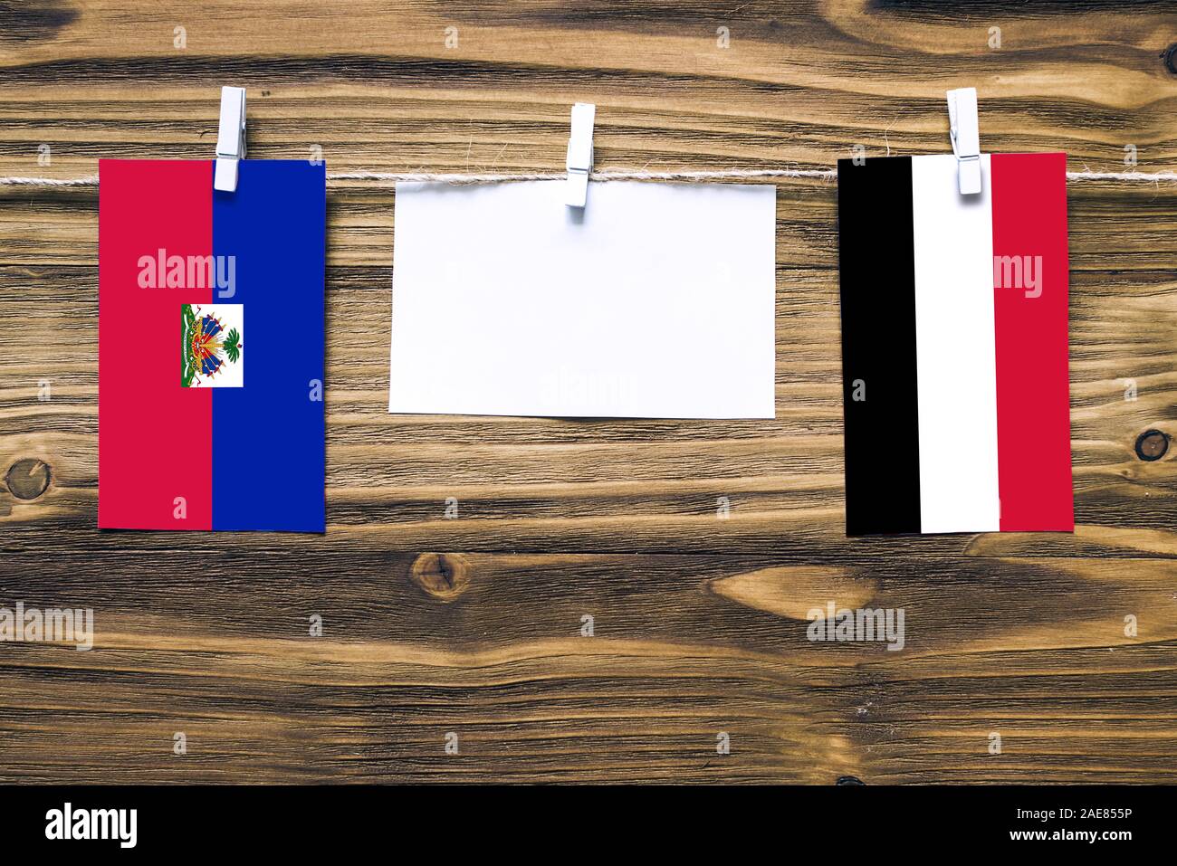 Hanging flags of Haiti and Yemen attached to rope with clothes pins with copy space on white note paper on wooden background.Diplomatic relations betw Stock Photo