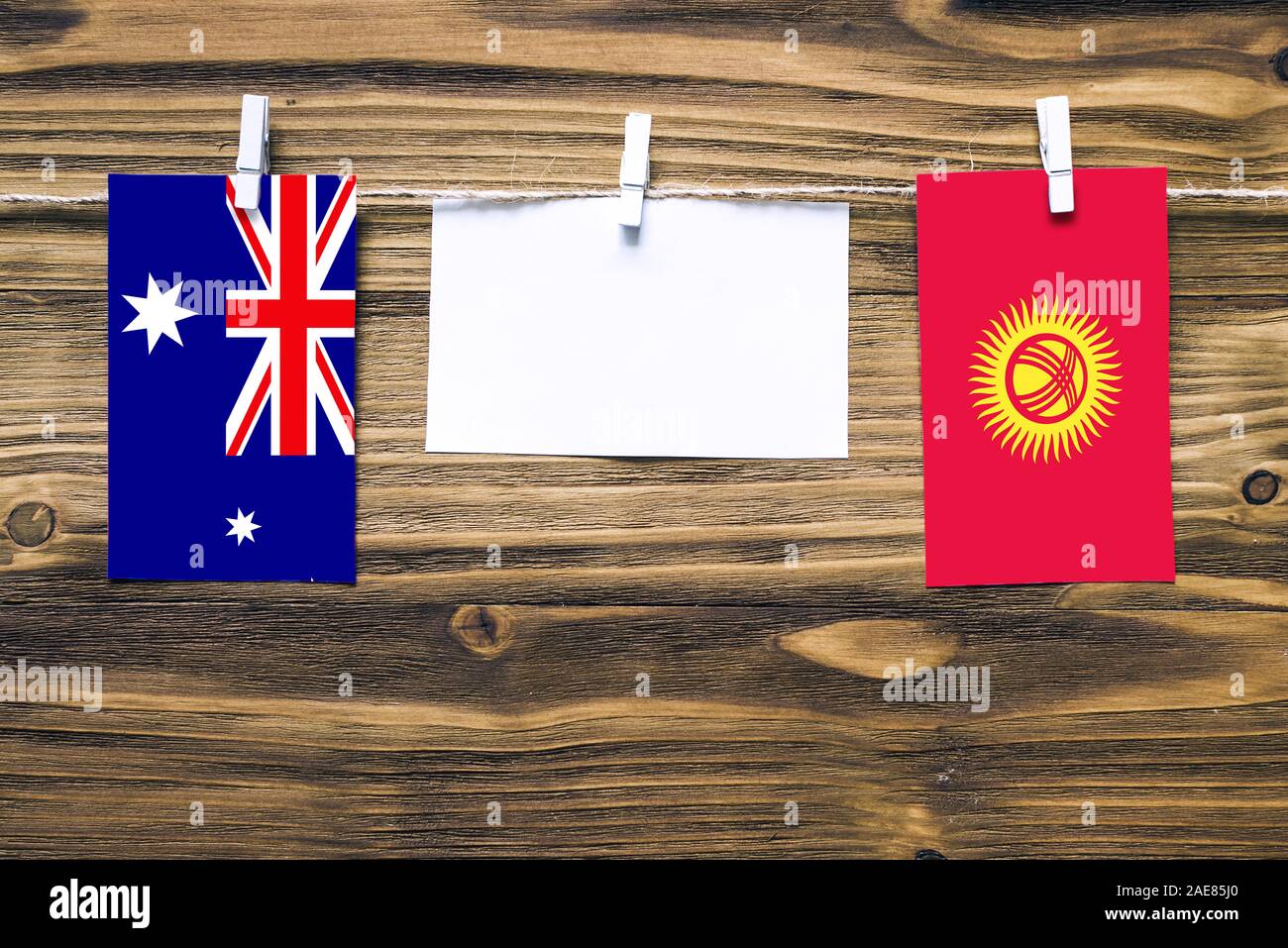 Hanging flags of Heard and Mcdonald Islands and Kyrgyzstan attached to rope with clothes pins with copy space on white note paper on wooden background Stock Photo