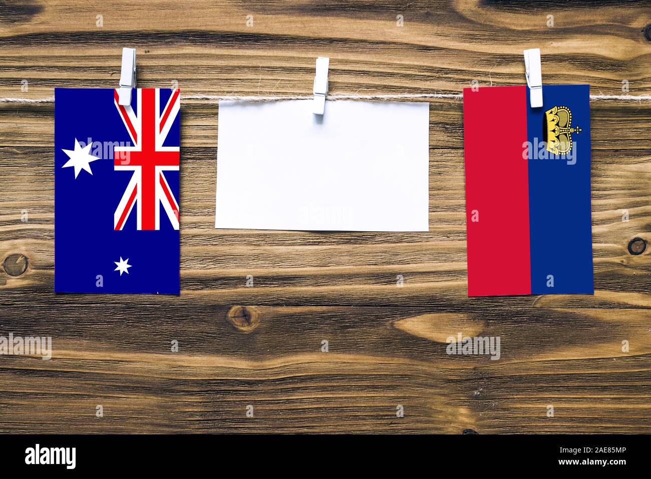 Hanging flags of Heard and Mcdonald Islands and Liechtenstein attached to rope with clothes pins with copy space on white note paper on wooden backgro Stock Photo