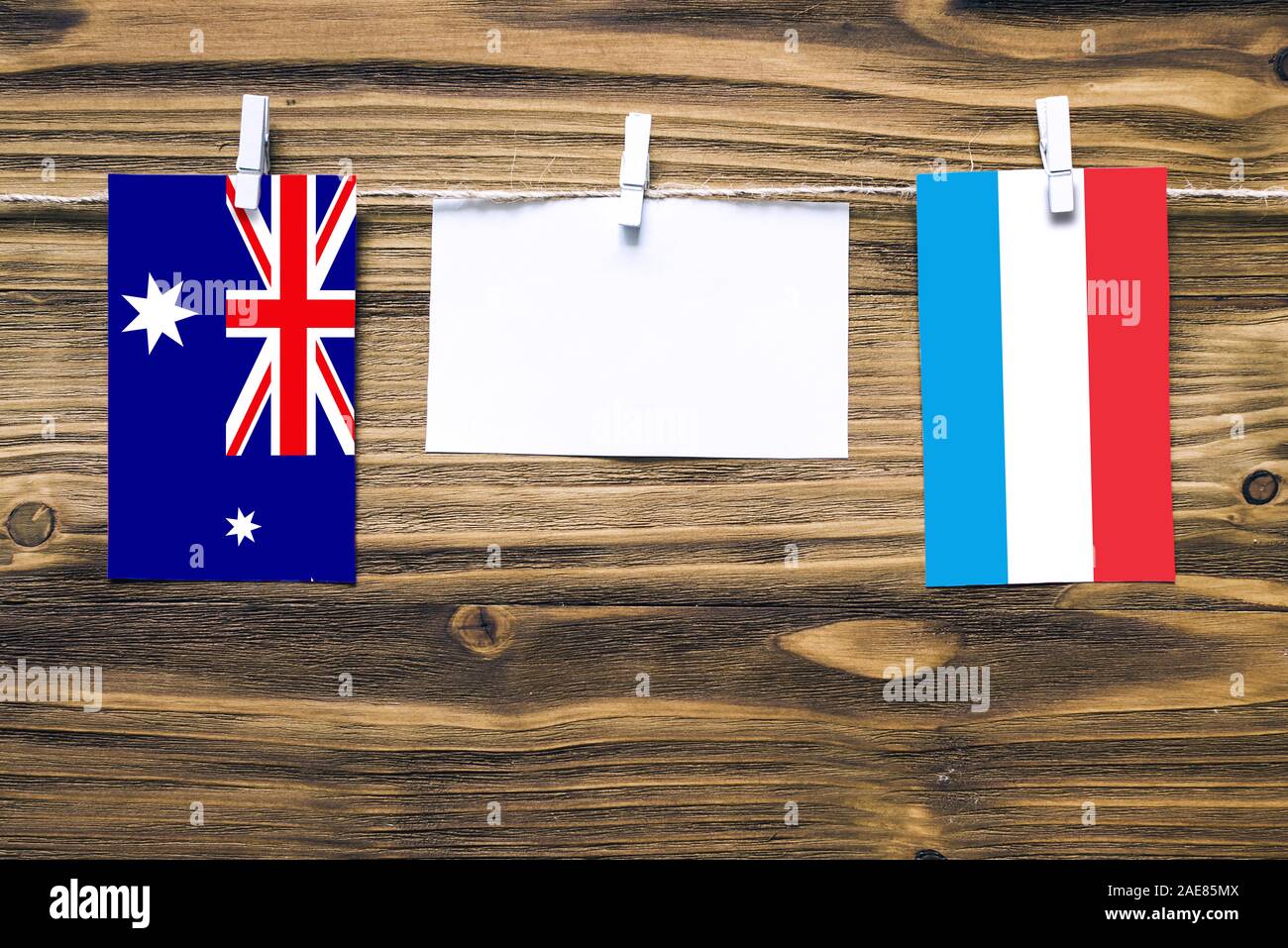 Hanging flags of Heard and Mcdonald Islands and Luxembourg attached to rope with clothes pins with copy space on white note paper on wooden background Stock Photo