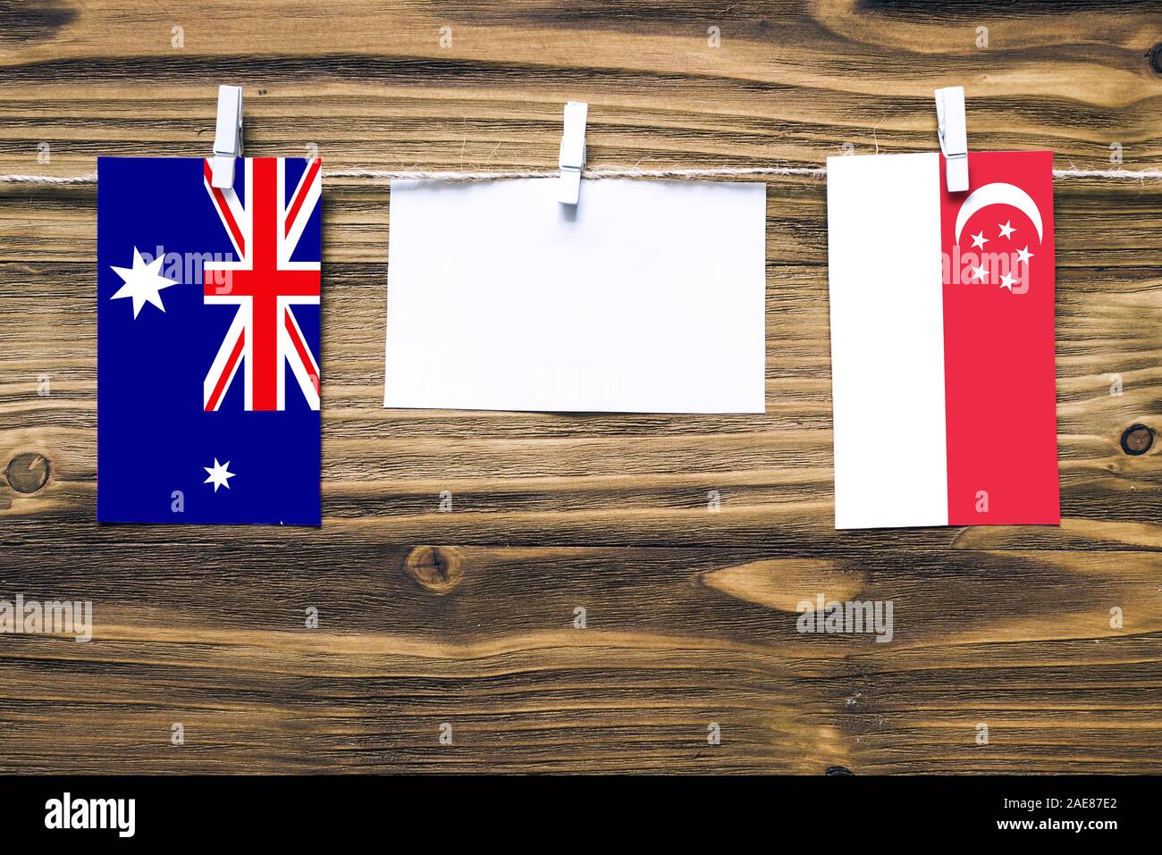 Hanging flags of Heard and Mcdonald Islands and Singapore attached to rope with clothes pins with copy space on white note paper on wooden background. Stock Photo