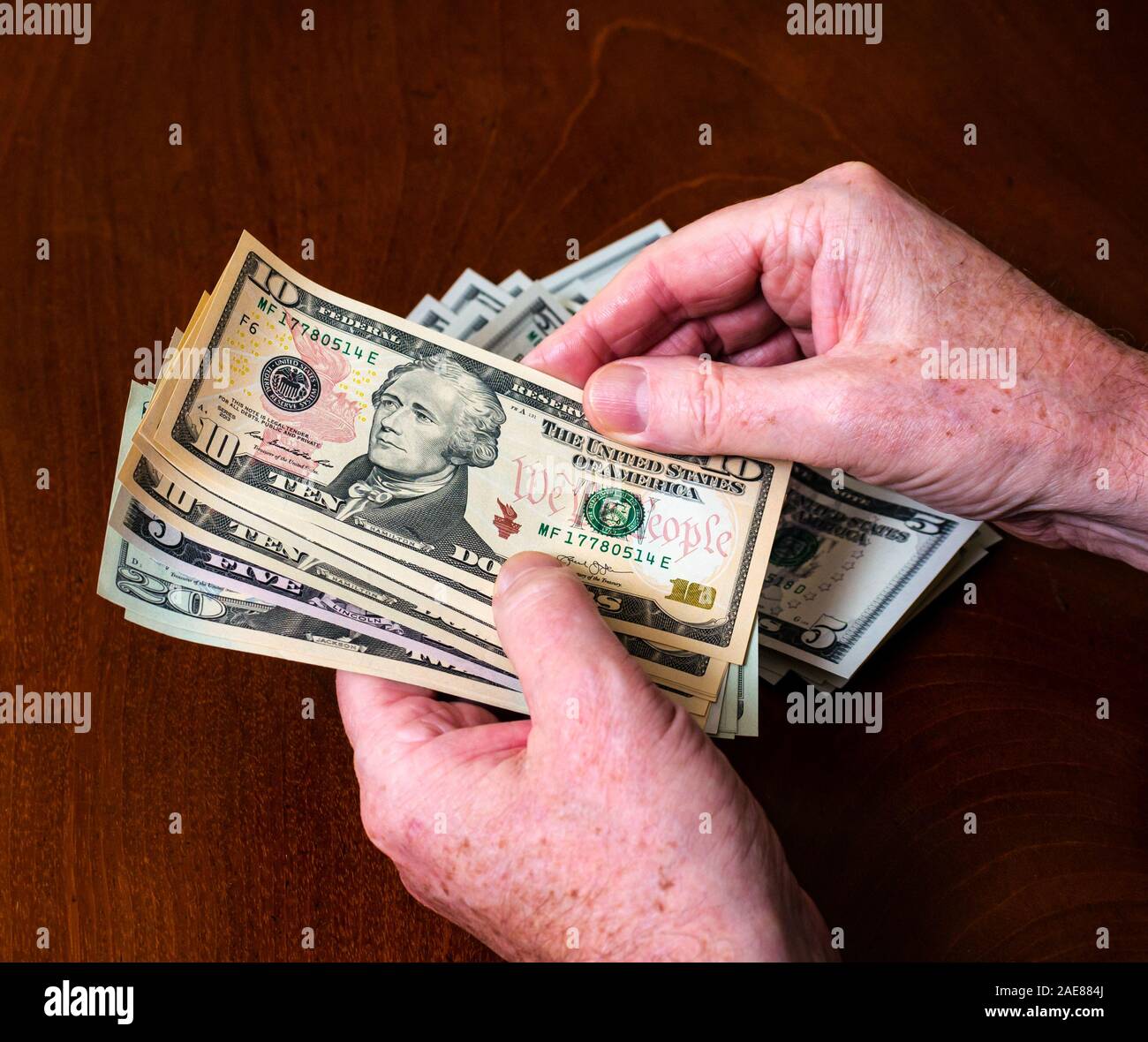 Man's hands counting American (US) money with five, ten & twenty dollar bills with US president Alexander Hamilton Stock Photo