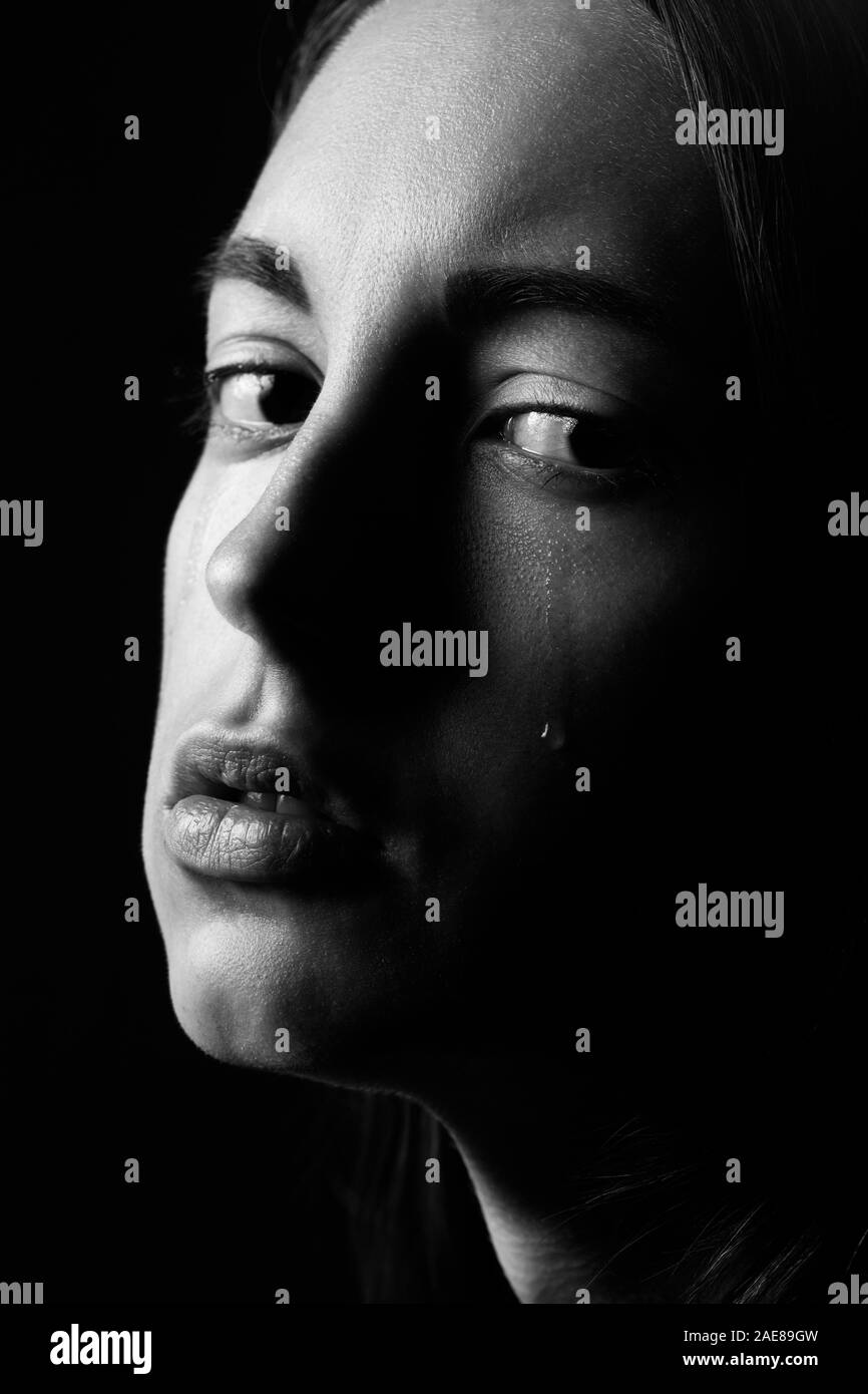 sad young woman crying on black background, looking at camera, closeup portrait, monochrome Stock Photo