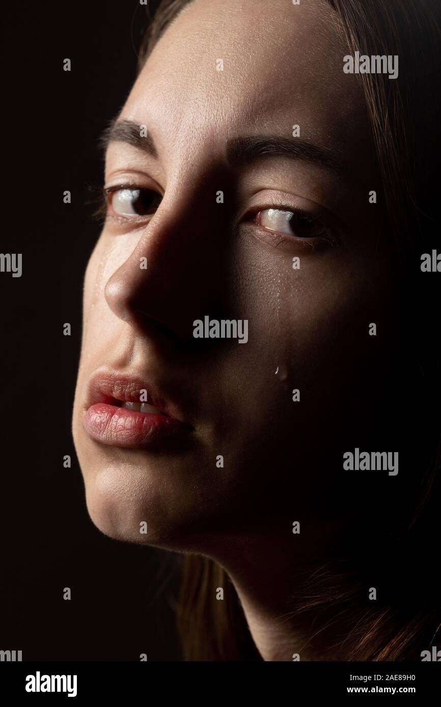 sad young woman crying on black background, looking at camera, closeup portrait Stock Photo