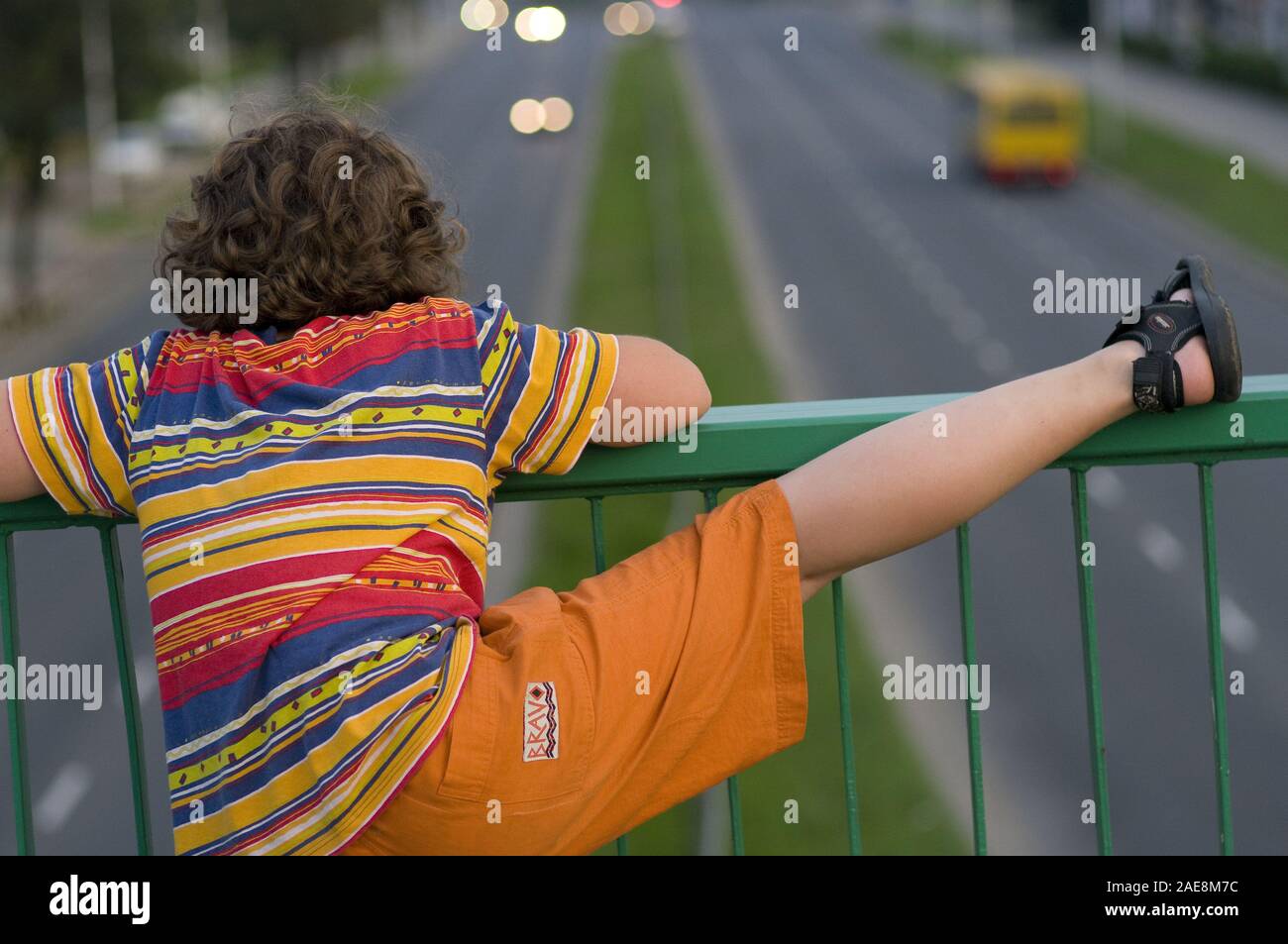 Boy on the footbridge over the street, resting his foot on the balustrade Stock Photo