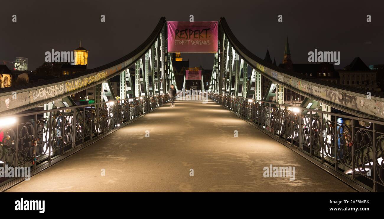 Straight view of illuminated Eisener Steg at night (panorama). Historical pedestrian bridge crossing Main river,  Construction with steel supports. Stock Photo