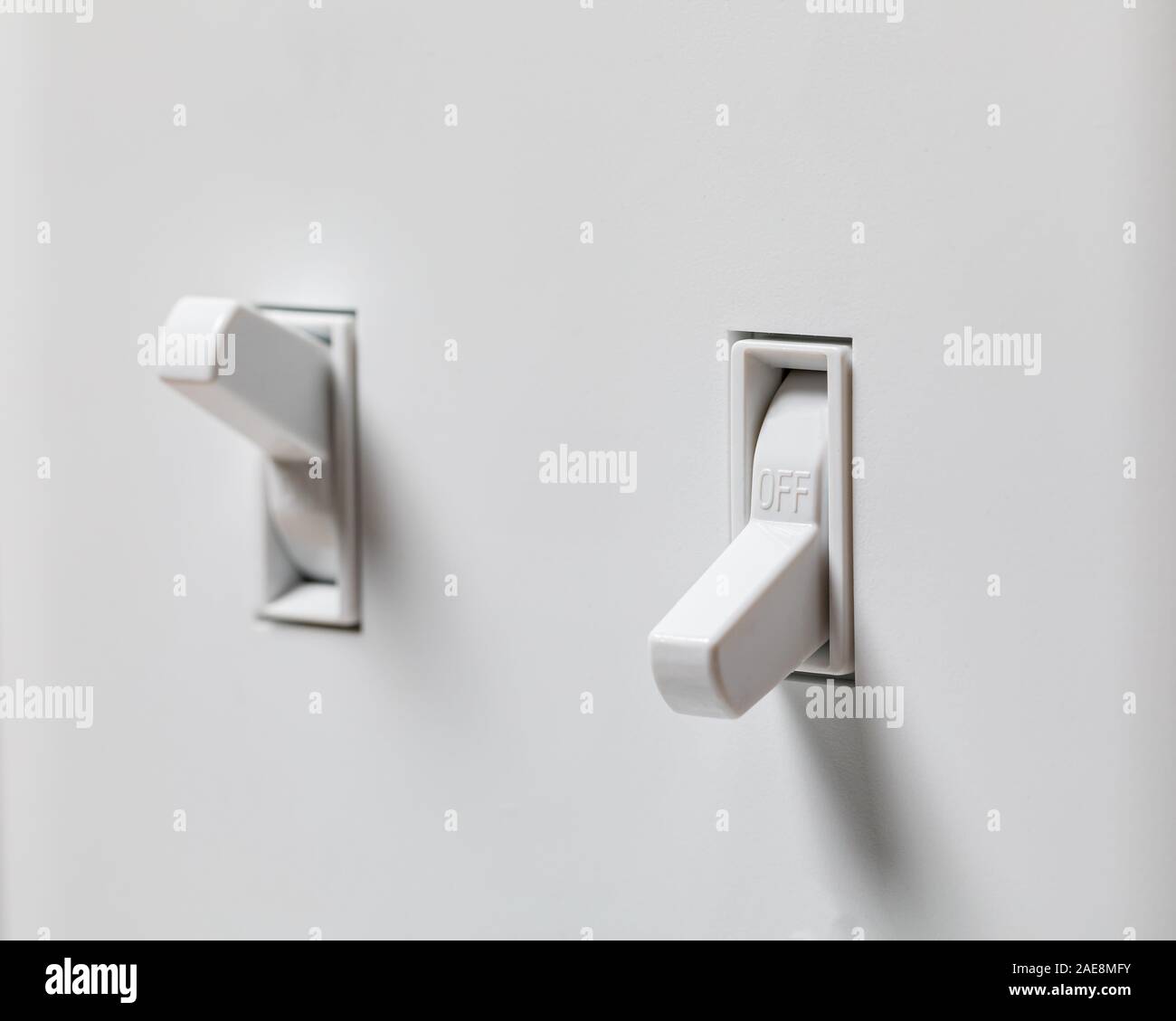 Closeup of white light switch turned off and another turned on in background with duplex wall plate. Concept of energy savings and conservation Stock Photo