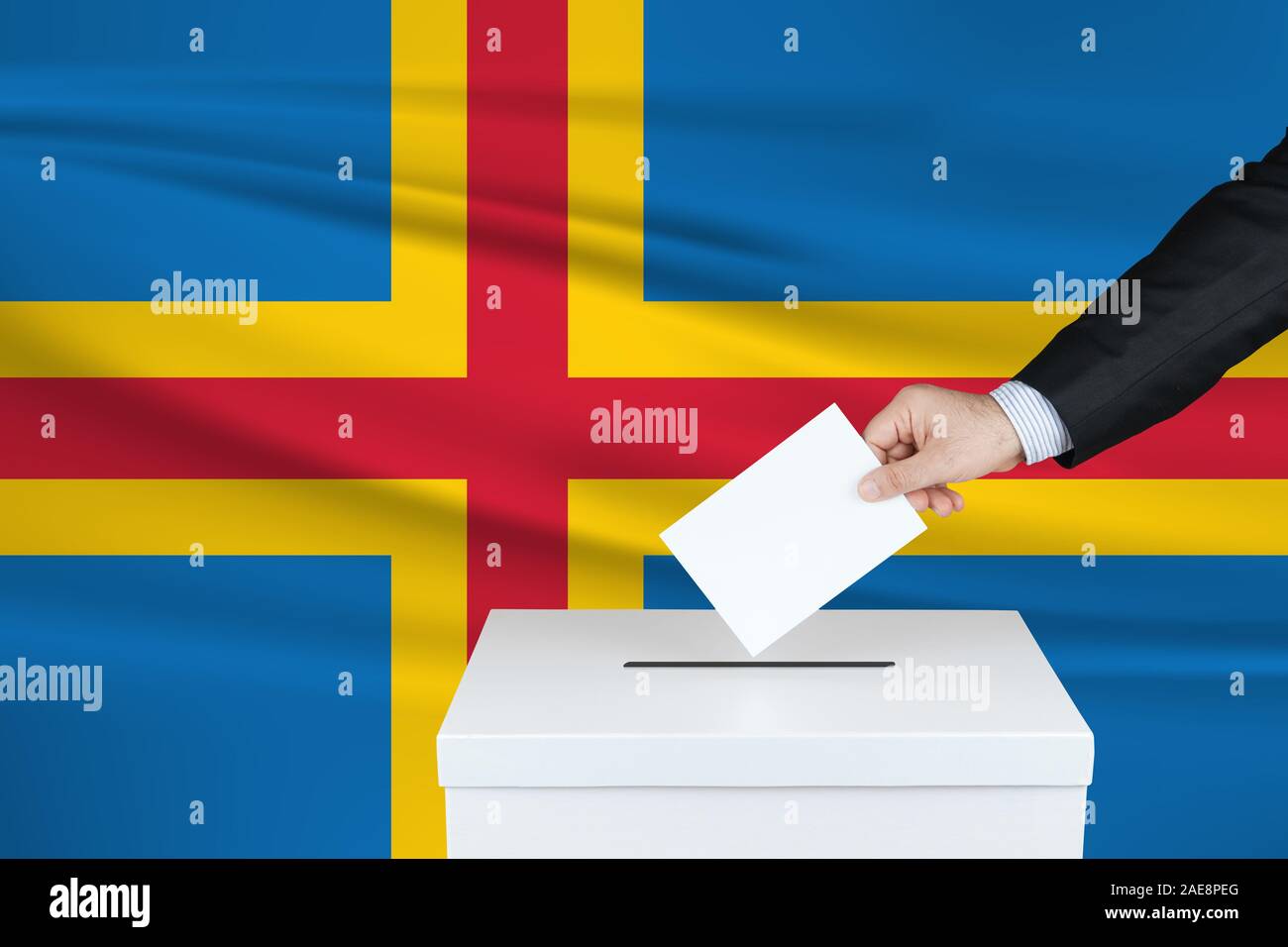 Election in Aland. The hand of man putting his vote in the ballot box. Waved Aland flag on background. Stock Photo