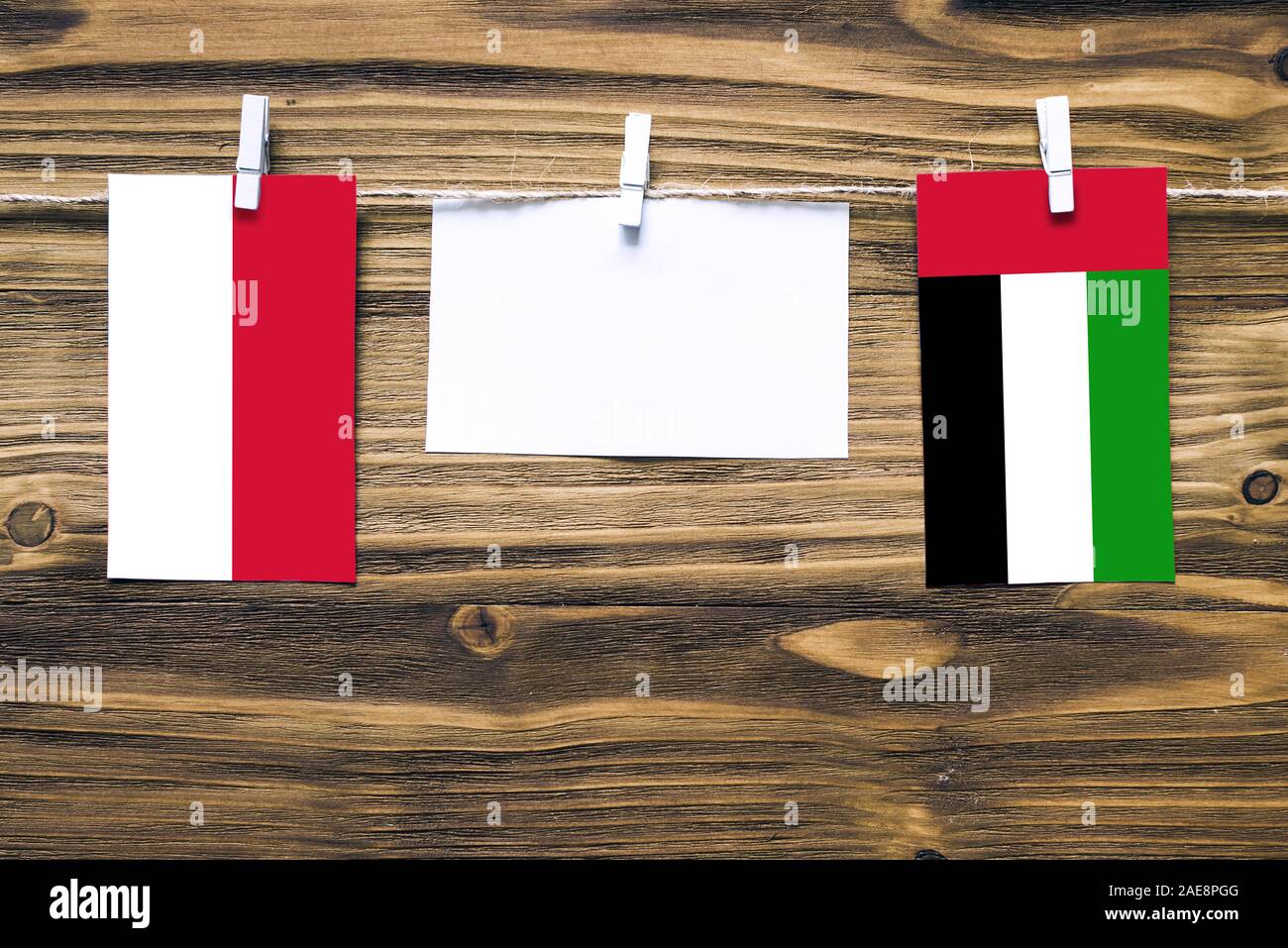 Hanging flags of Indonesia and United Arab Emirates attached to rope with clothes pins with copy space on white note paper on wooden background.Diplom Stock Photo