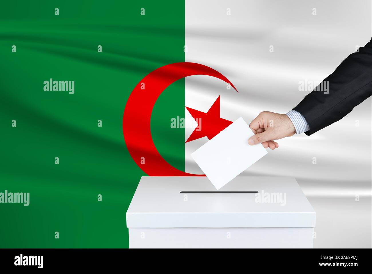 Election in Algeria. The hand of man putting his vote in the ballot box. Waved Algeria flag on background. Stock Photo