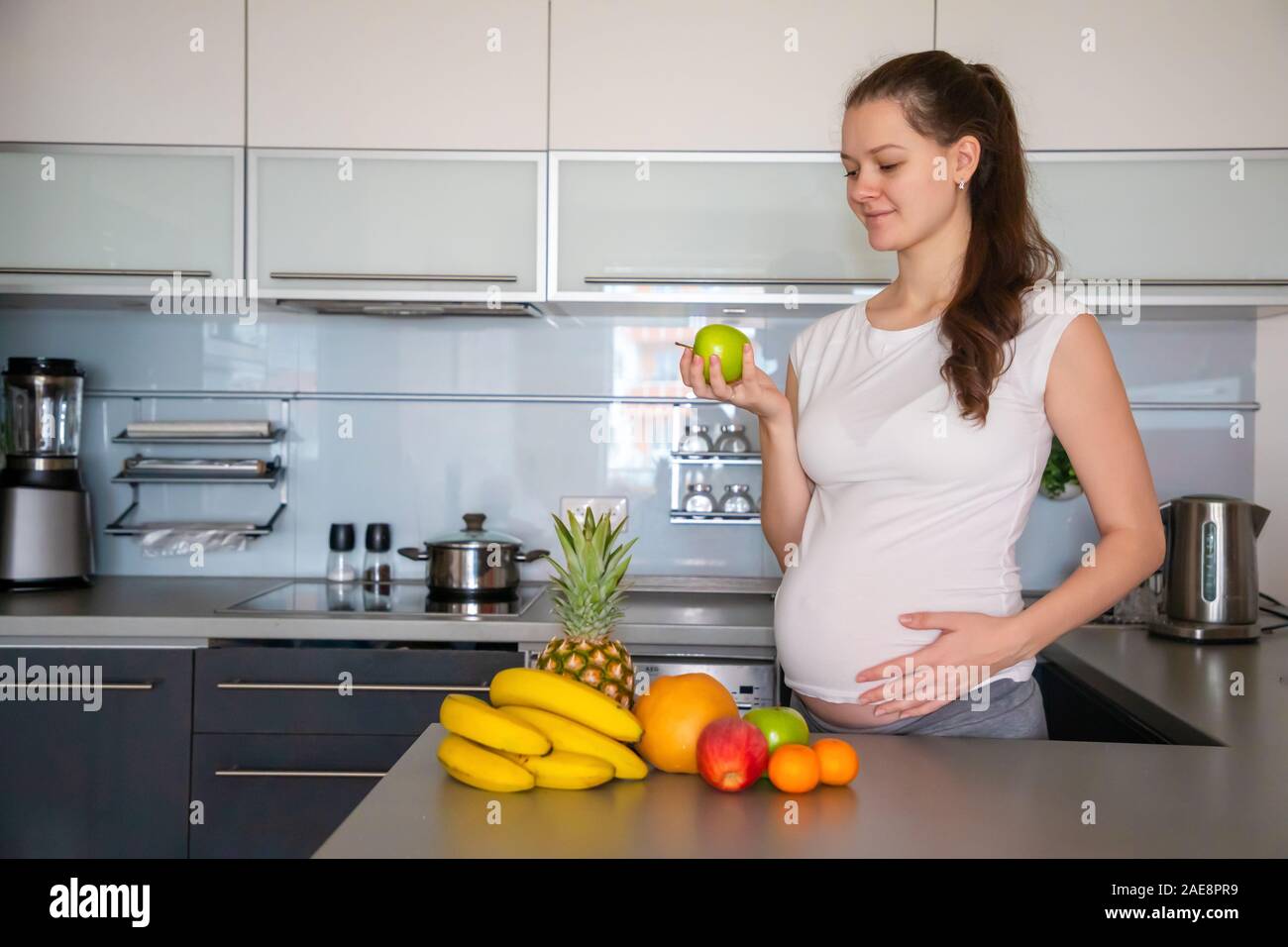Pregnant woman and different tropical fruits in home kitchen Stock