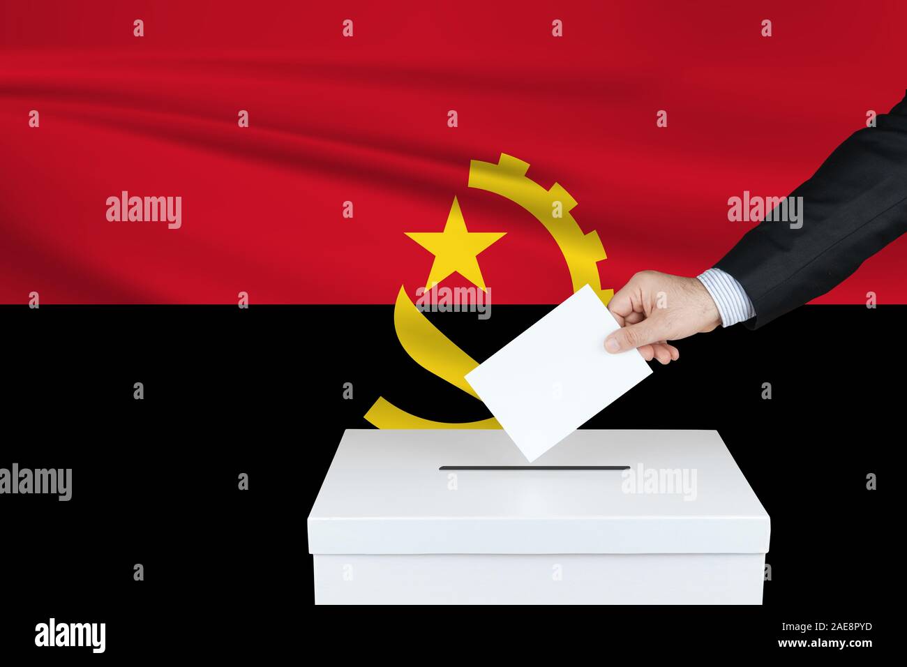 Election in Angola. The hand of man putting his vote in the ballot box. Waved Angola flag on background. Stock Photo