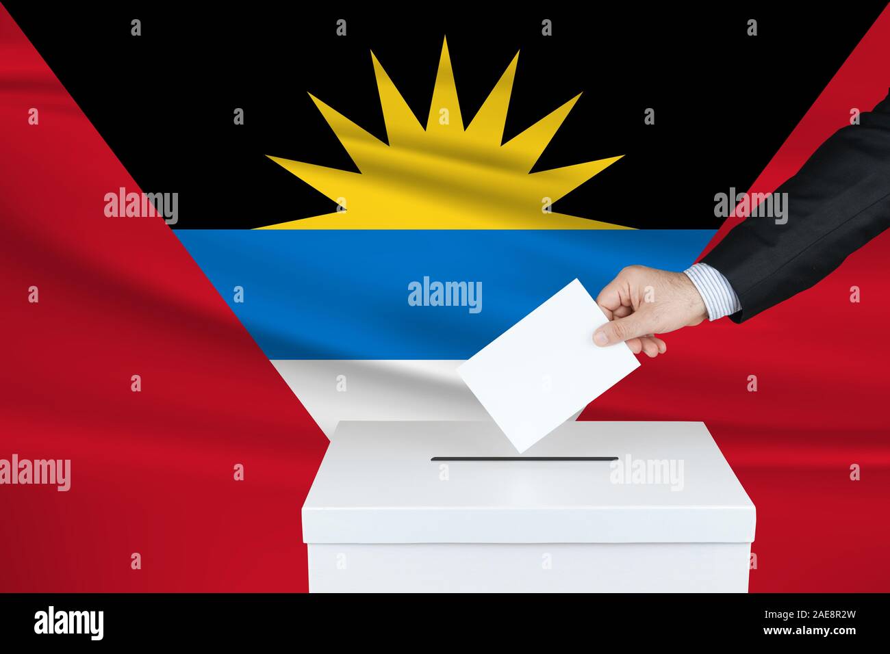 Election in Antigua. The hand of man putting his vote in the ballot box. Waved Antigua flag on background. Stock Photo