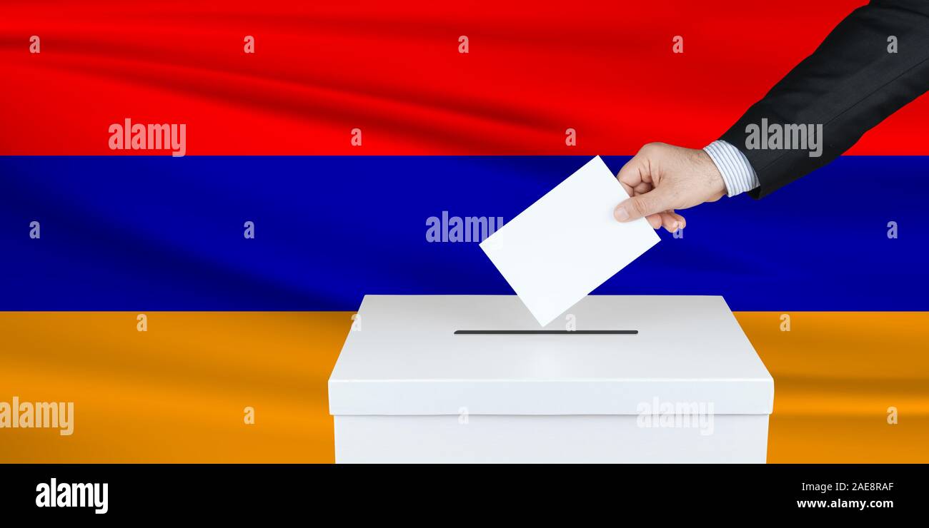 Election in Armenia. The hand of man putting his vote in the ballot box. Waved Armenia flag on background. Stock Photo