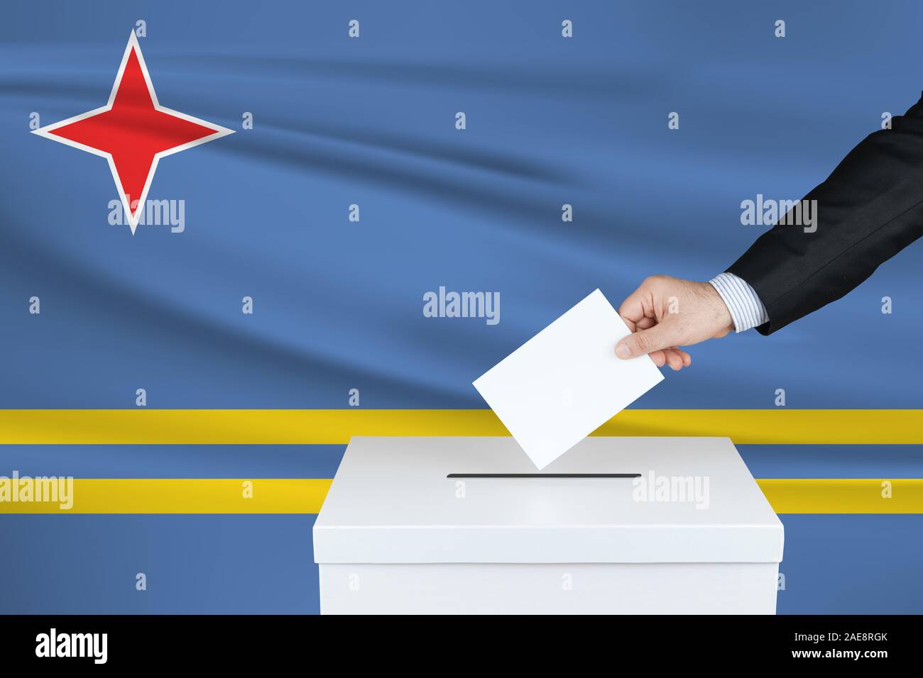 Election in Aruba. The hand of man putting his vote in the ballot box. Waved Aruba flag on background. Stock Photo