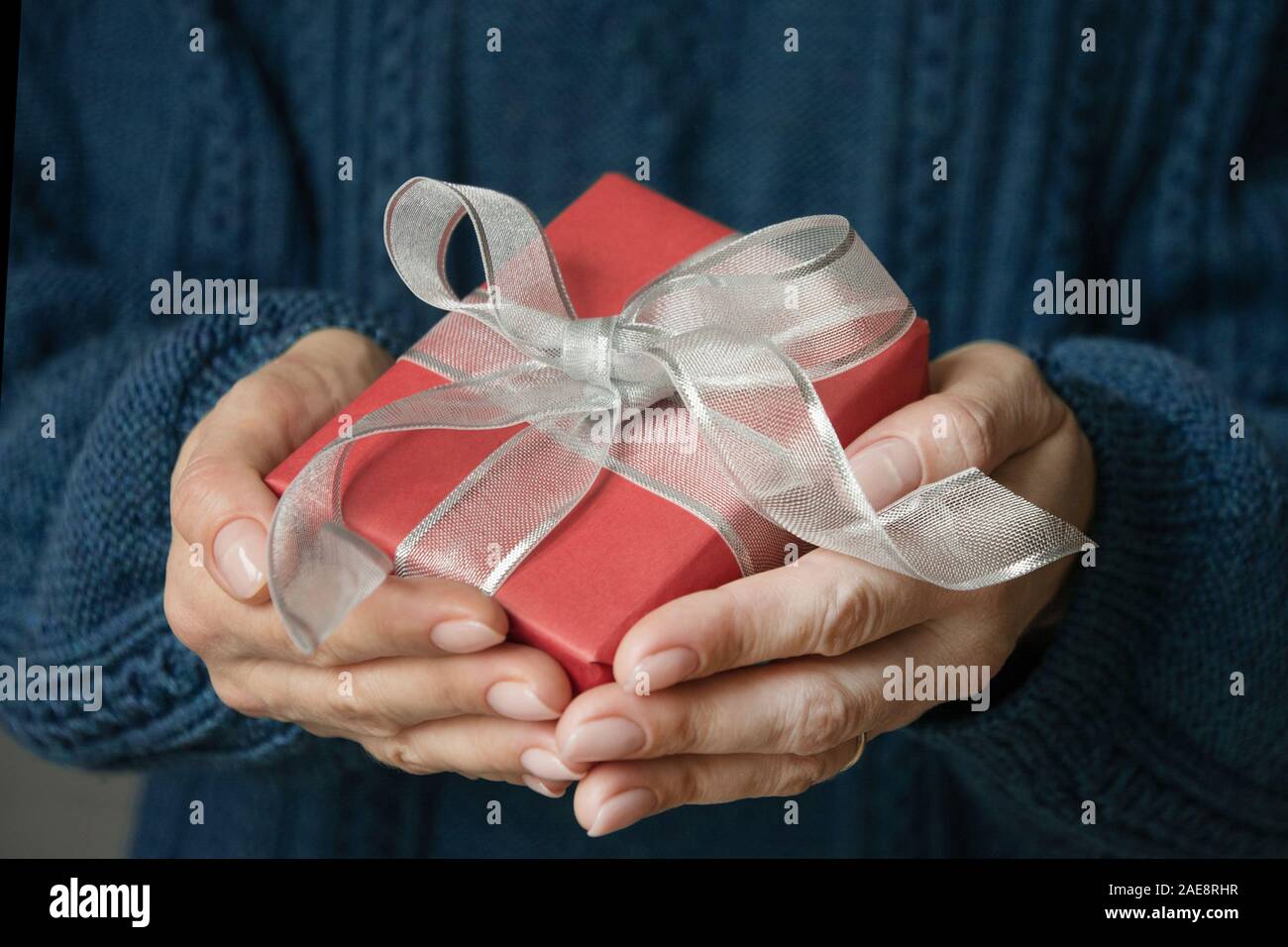 Female hands holding Christmas gift in blue cozy sweater. Xmas present. Boxing day. Xmas present. Boxing day. Close up. Stock Photo